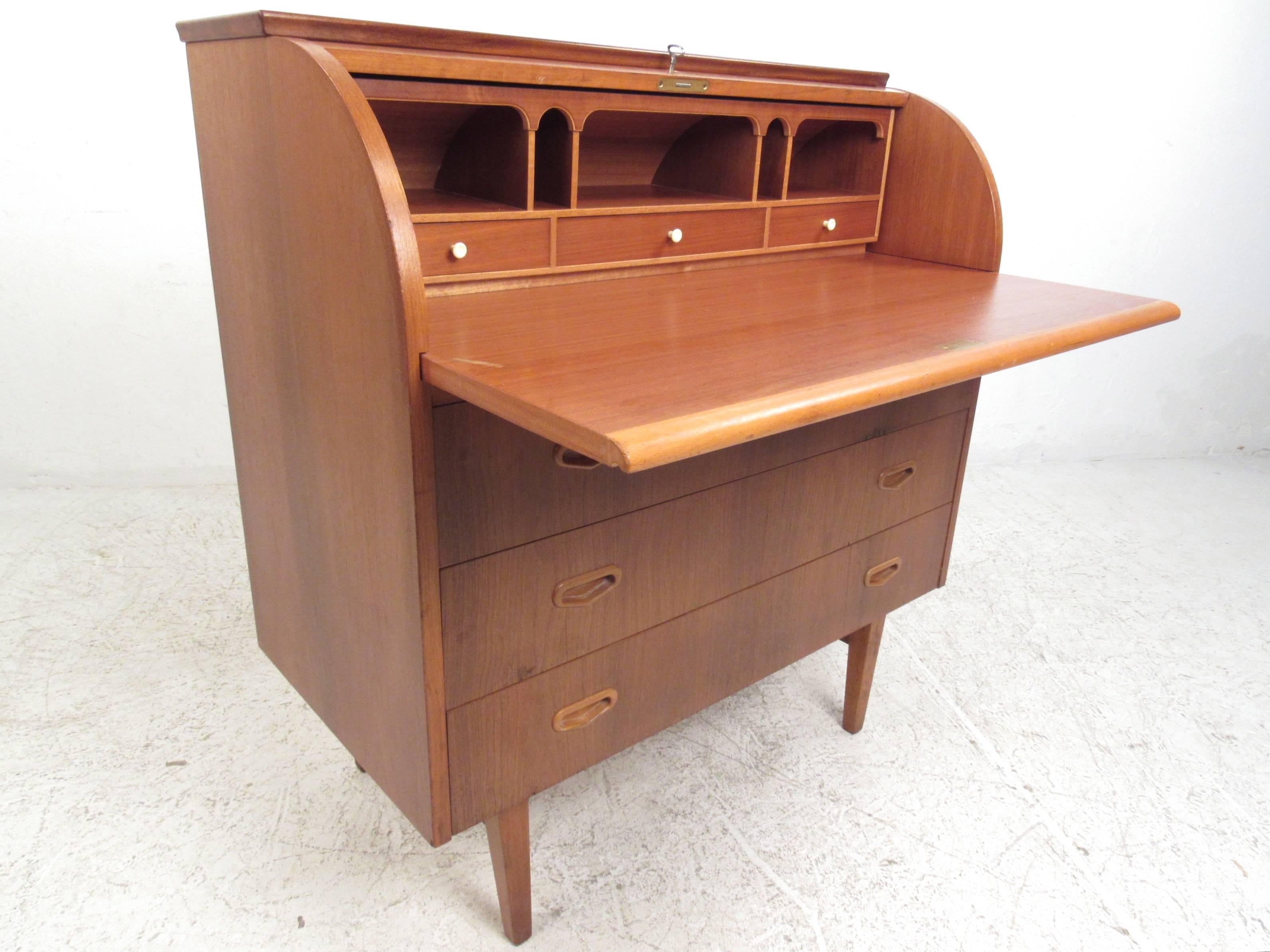 This vintage teak roll top secretary desk provides a stylish yet compact workspace in any setting. Three spacious drawers feature carved teak handles, while the locking roll-top compartment features a pull-out writing table and multiple shelves for