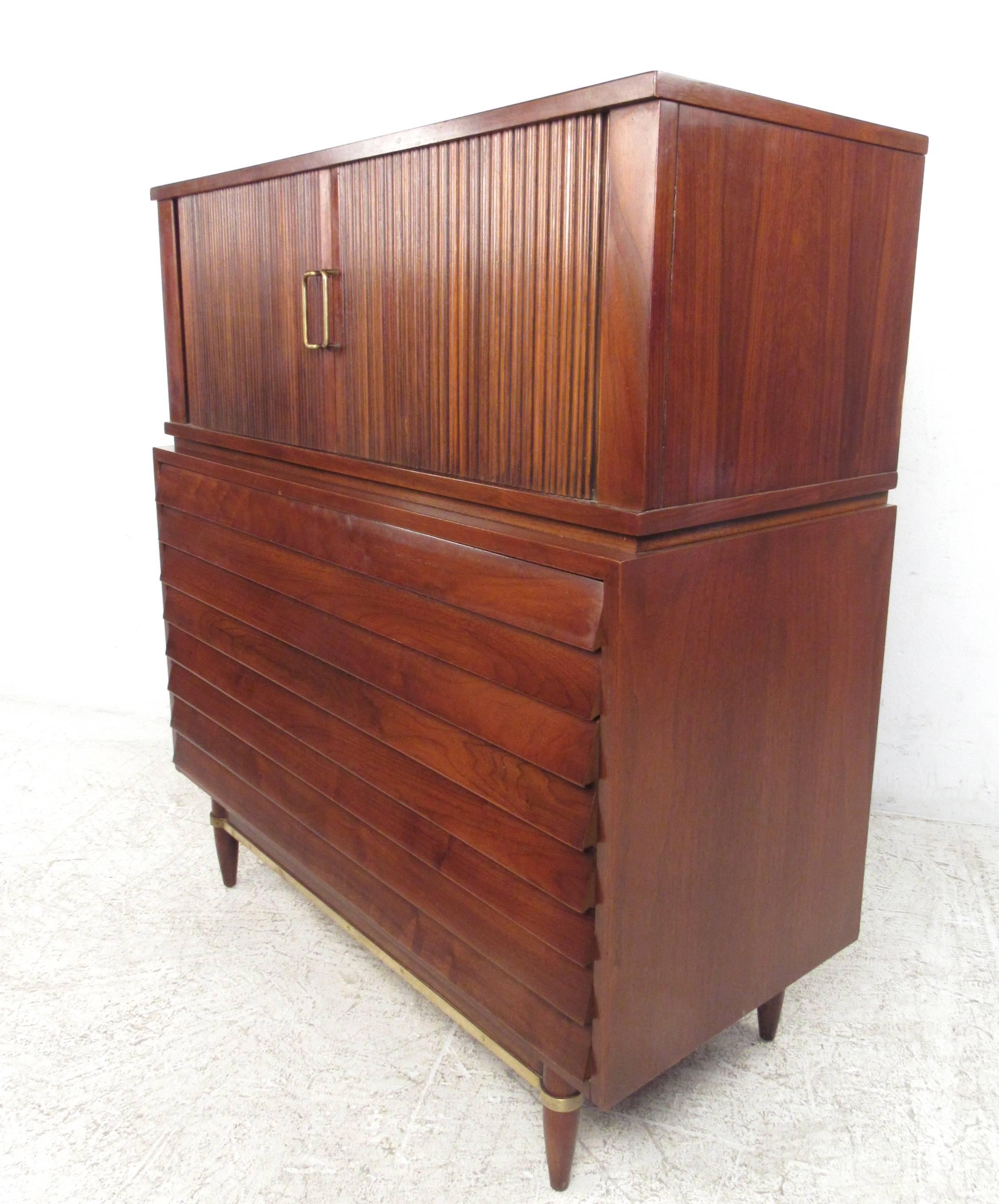 This Mid-Century Modern walnut highboy dresser features truly unique vintage design details, including louvered front drawers, horizontal tambour doors, and brass trim stretchers. This stunning dresser features five spacious drawers for organization