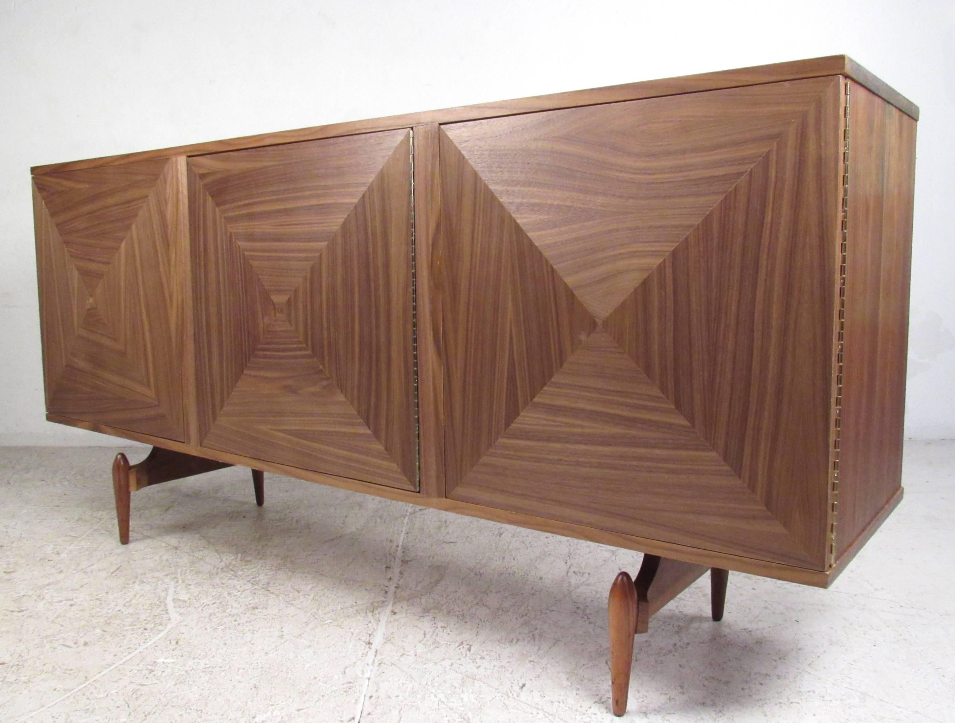 This Mid-Century style storage credenza features three spacious interior cabinets with fittings for adjustable shelves. Stylish sculpted front natural finish cabinet doors are wonderfully accented by vintage tapered legs on base. Please confirm item