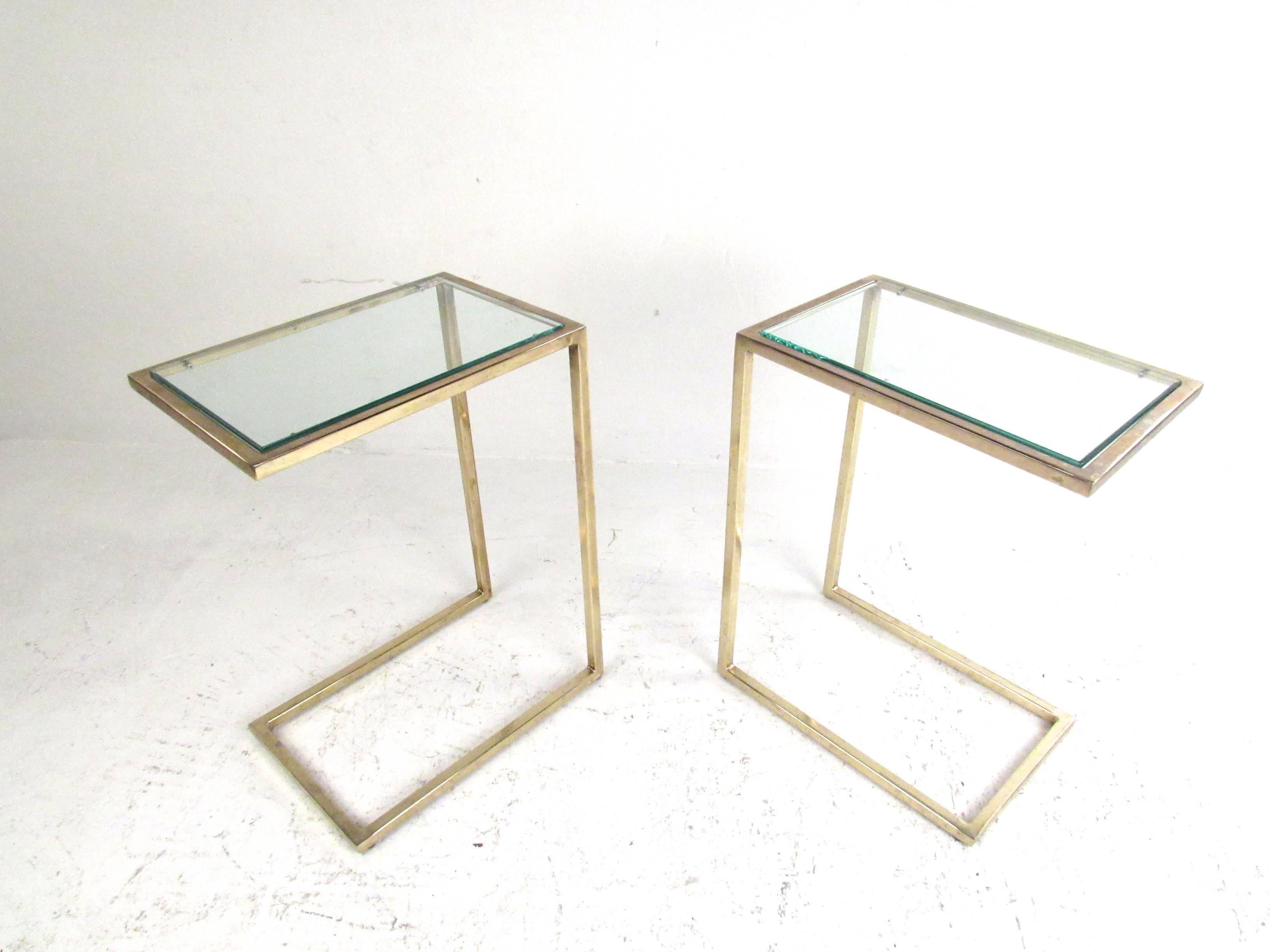 This stunning pair of Mid-Century end tables features a unique narrow size with elegant design. Heavy vintage brass pairs wonderfully with raised glass tops, while the unique shape of the piece provide simple yet stylish tables for a variety of