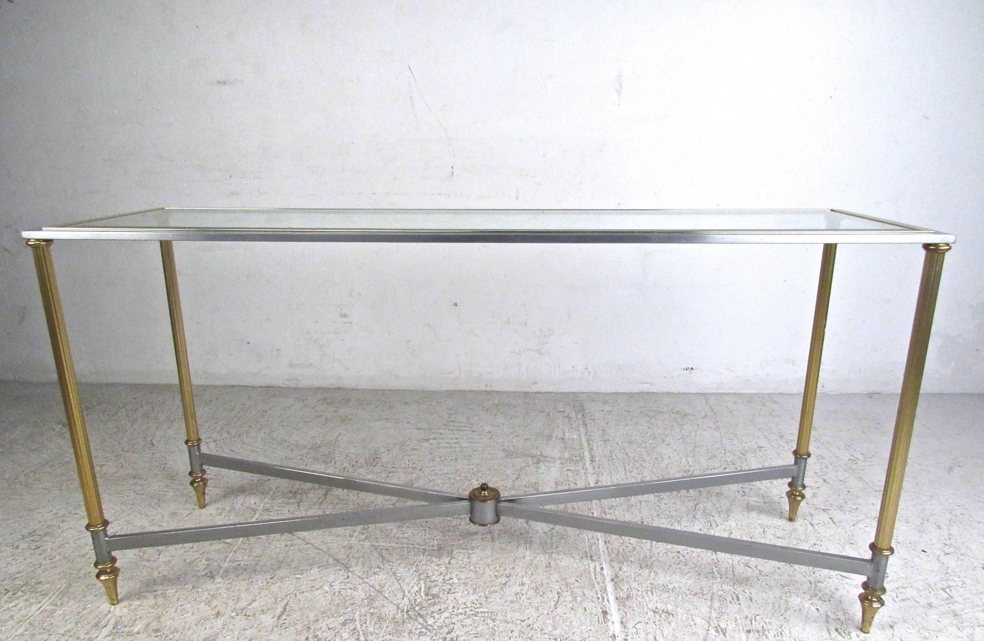 This unique vintage console table features a stunning slim design with unique brass legs and trim. Ornate tapered feet, grooved frame, and beveled glass top add to the beauty of this Mid-Century hall table in the style of Maison Jansen. Perfect