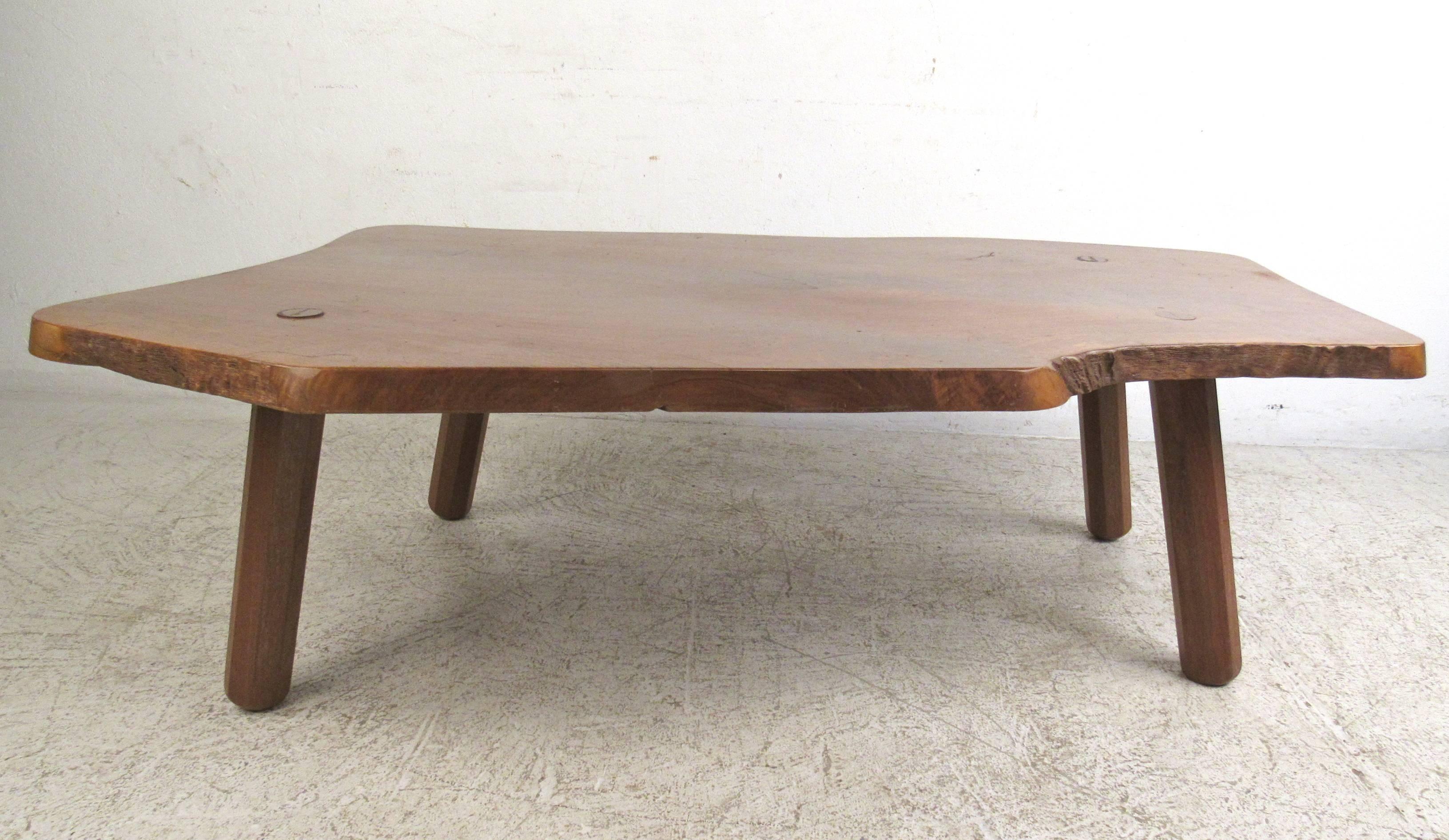This Mid-Century live edge coffee table features a thick tree slab top mounted on hardwood legs. Wonderful vintage rustic appeal makes this large and uniquely shaped coffee table a visually impressive addition to a variety of interiors. Please