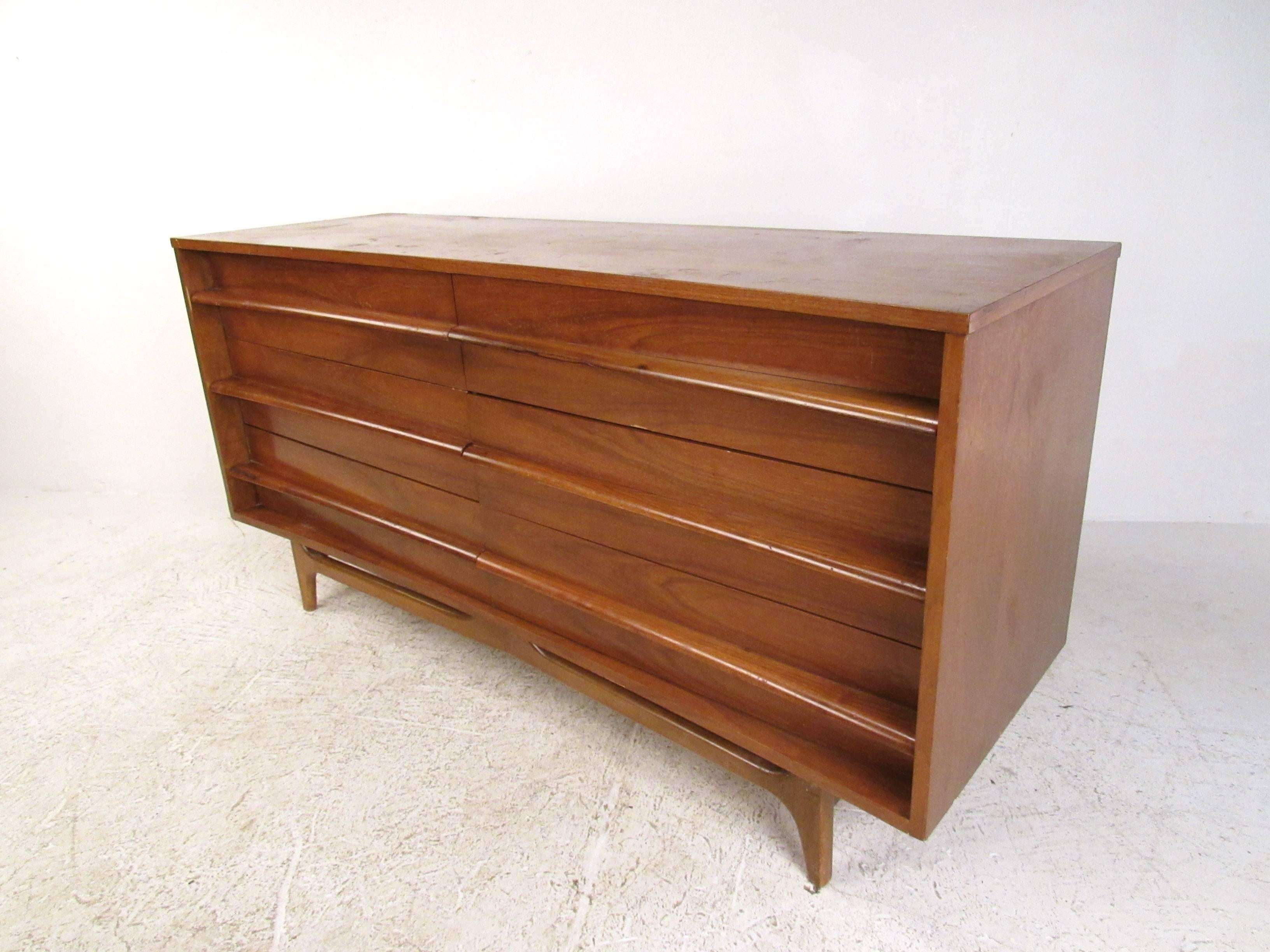 This classic Mid-Century dresser features a rich natural walnut finish and simple straight lines. Set of six drawers offers plenty of storage while it's unique tapered leg base and carved drawer pulls add to its vintage appeal. Please confirm item