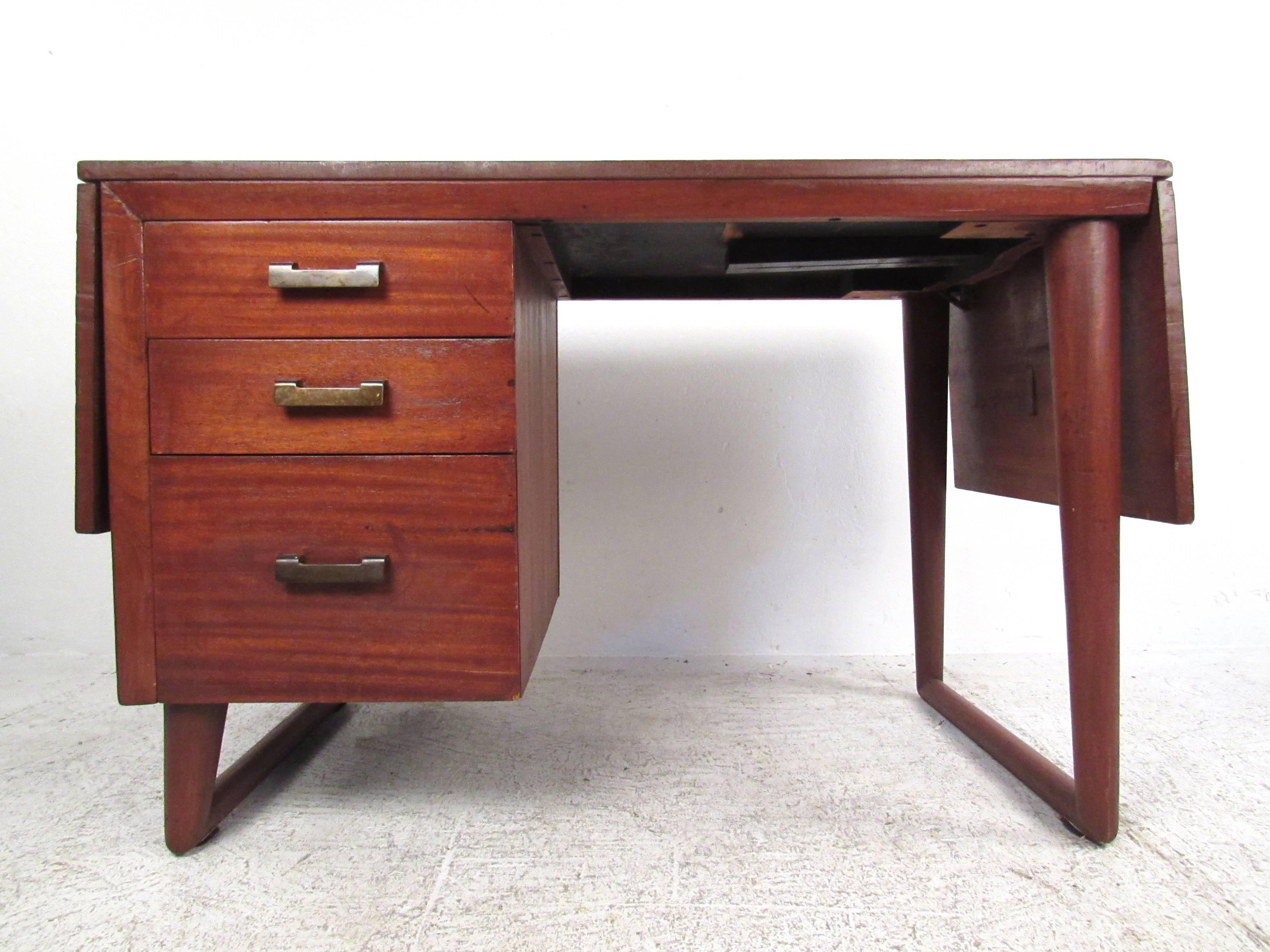 This unusual drop-leaf writing desk features sculptural sled legs, wide brass finish handles, and a Dual drop leaf design that expands the 44 inch workspace out to 72 inches. Three drawers for storage make this a versatile desk for a variety of