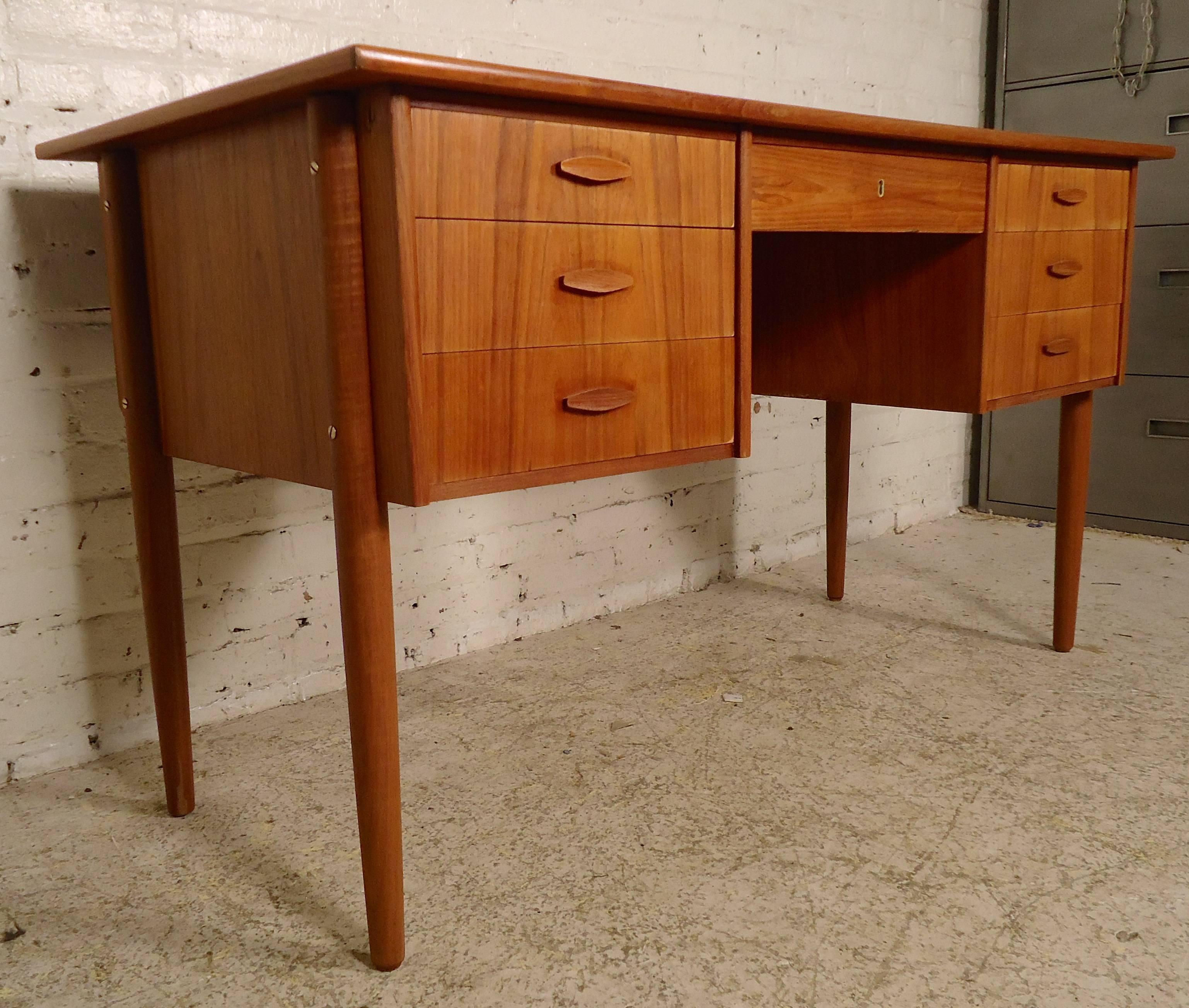 Simple and stylish Danish desk with teak grain, featuring seven drawers, wide top and long tapered legs. Sculpted handles on the dovetailed drawers and a finished back with storage add to the well-crafted Danish design.

Kneehole: 17.5 wide, 15