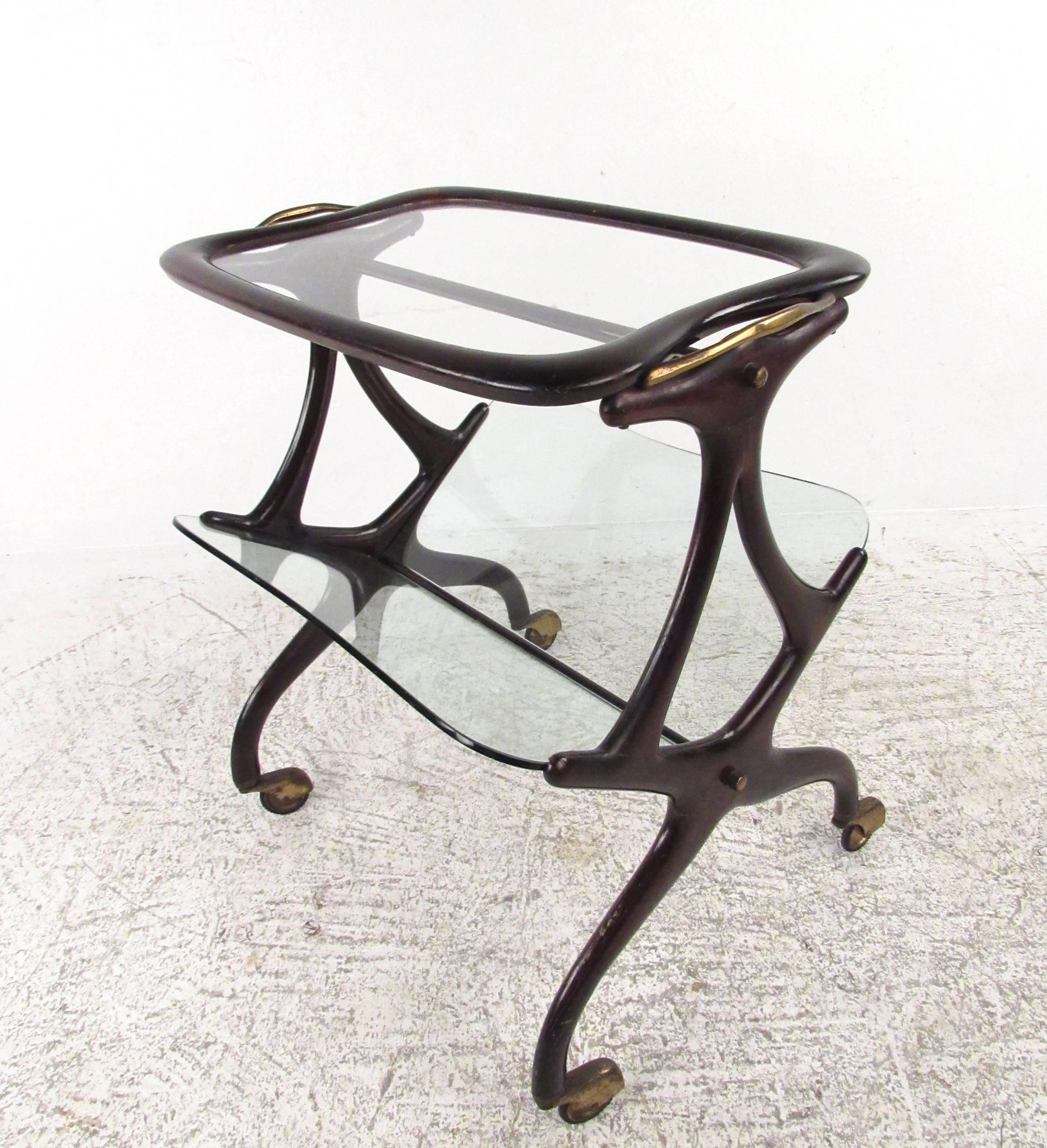 This beautiful Italian magazine cart features the unique sculptural Italian design of Cesare Lacca and makes a stunning addition to any interior. Perfect rolling side table with glass table top and lower tier magazine rack. Brass accents wonderfully