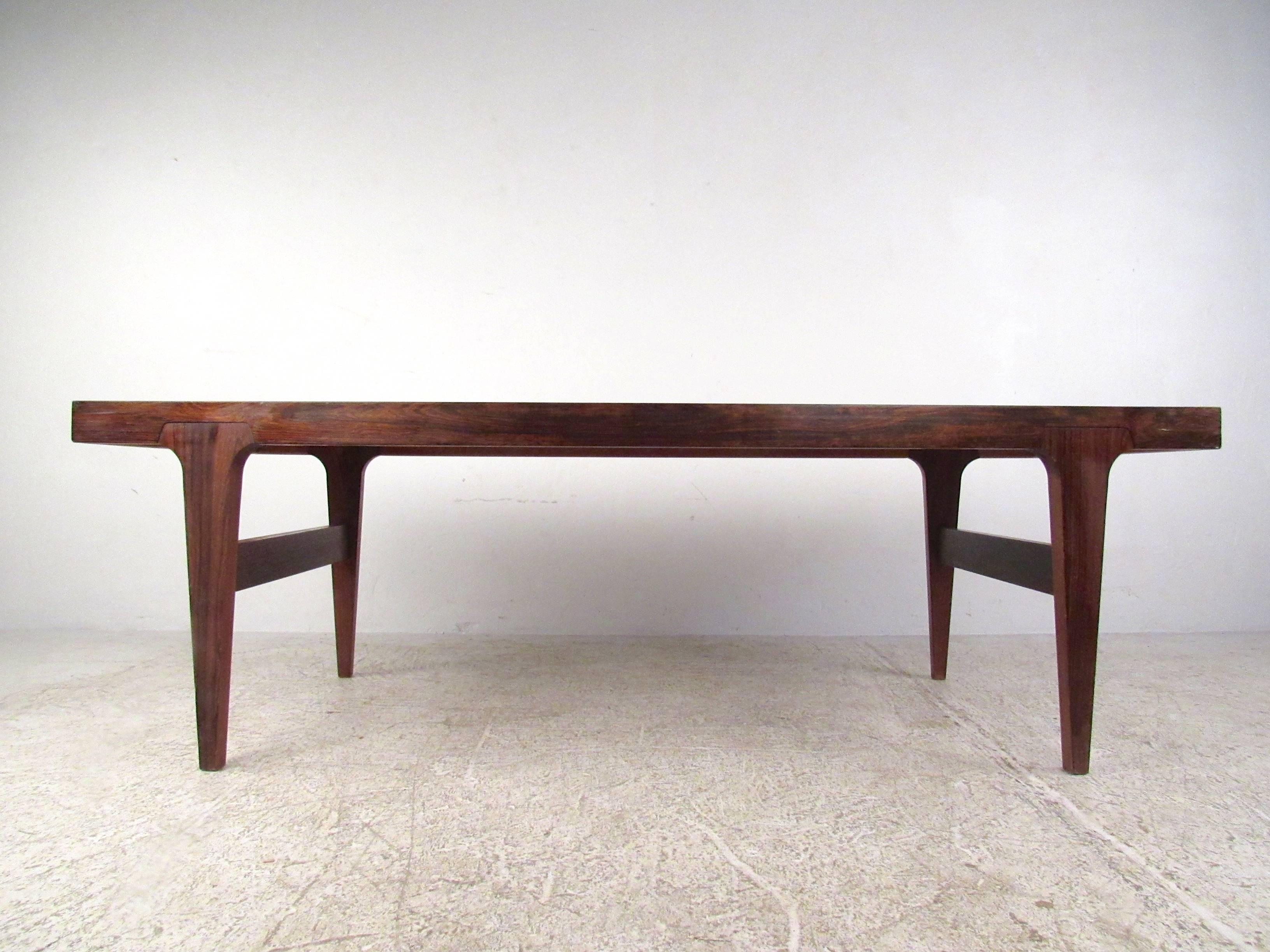 This beautiful mid-century Danish rosewood coffee table features unique tapered legs with wide slat stretchers for added support. The thick Mid-Century rosewood tabletop has a wonderful vintage finish and makes a unique addition to any interior.