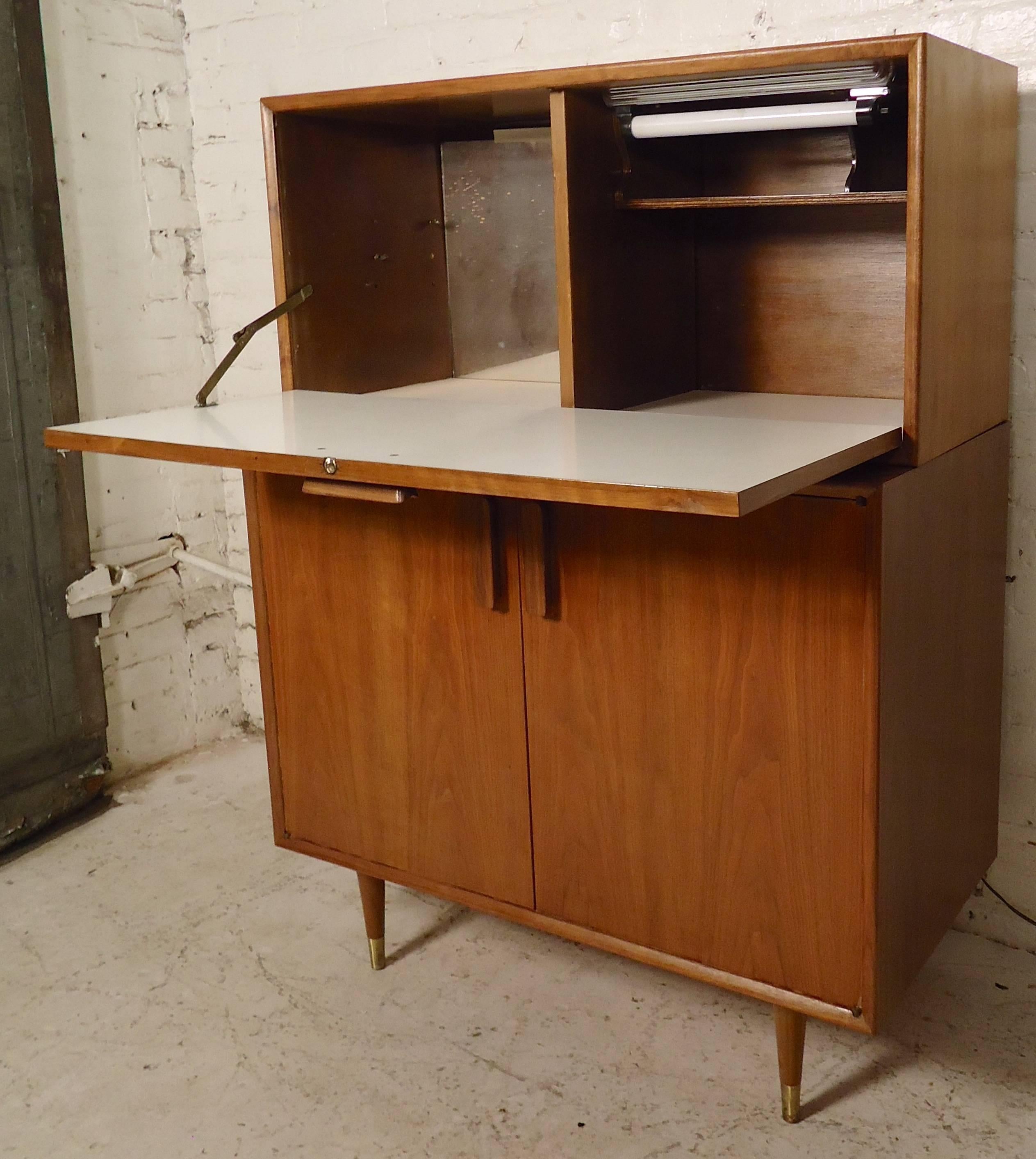 Vintage modern teak cabinet with drop front bar top. Very unique 1960s bar featuring mirrored back for glasses, lamp, bottom cabinet with adjustable shelf, sculpted handles and cone legs. Top rests on the bottom cabinet.

(Please confirm item