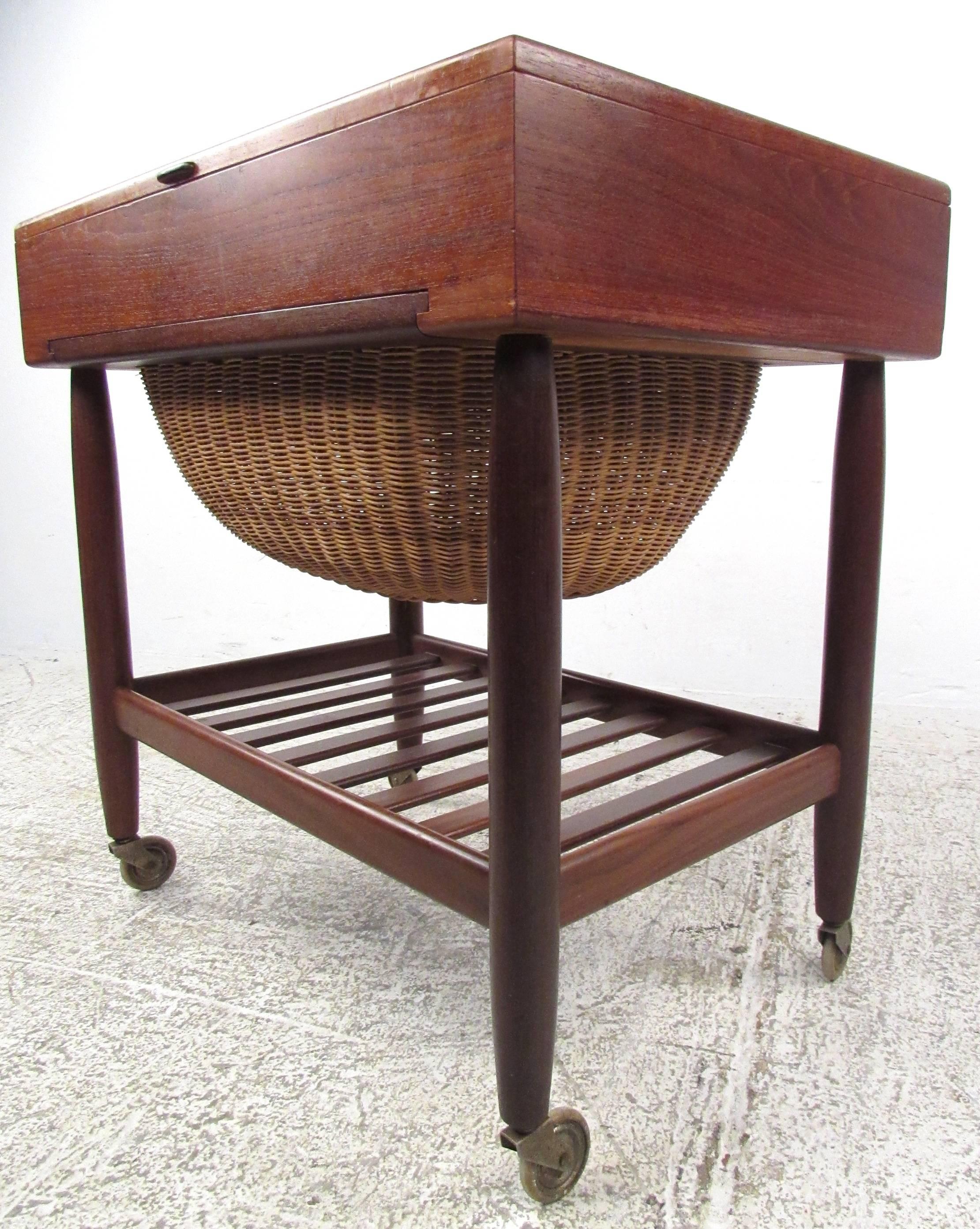 The wonderful Mid-Century Danish teak sewing basket is manufactured by Vitre of Denmark and attributed to Ejvind Johannson. The stylish design features a rosewood handle to access interior storage, while a lower shelf allows access to built in