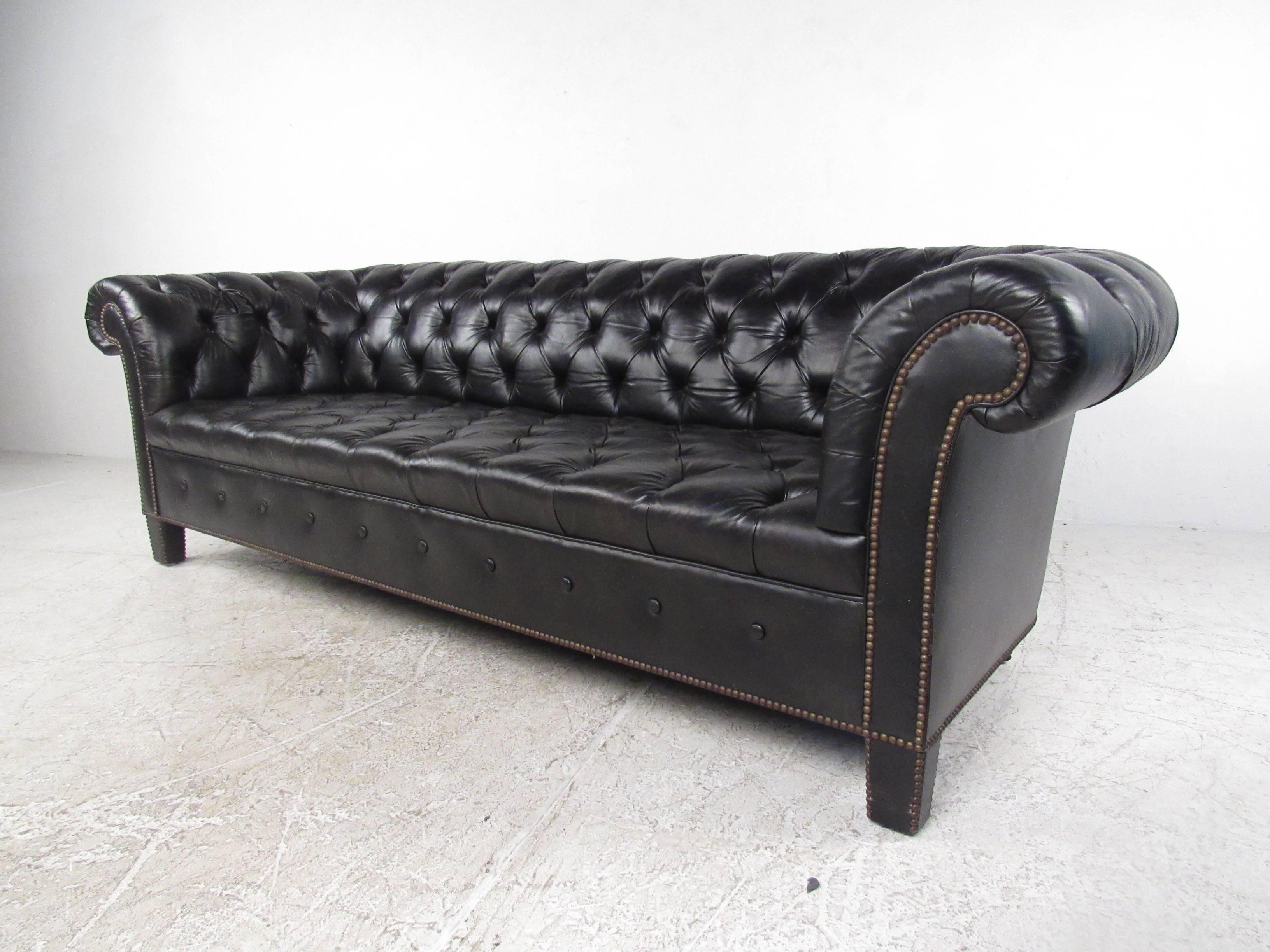 This beautiful vintage sofa by Baker Furniture features tufted black upholstery with brass nail heads, and scrolled arms. Sleek and stylish design in dark fabric makes this a unique piece, while wide four seat design makes this 1970s Mid-Century