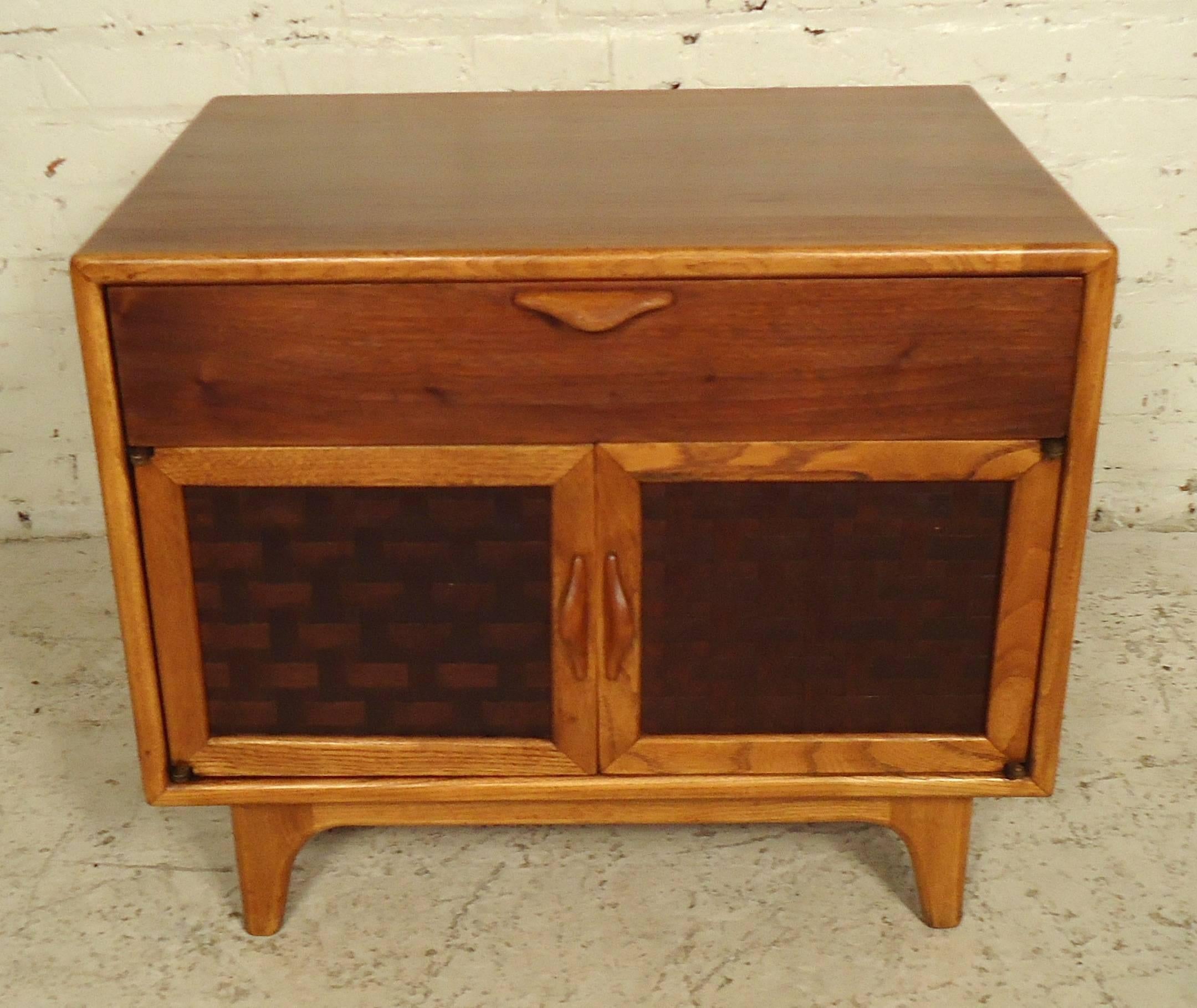 Elegant Mid-Century side table features a top drawer, bottom storage compartment and set of basket woven front doors on sturdy legs. Attractive oak and walnut accenting, as well as sculpted handles to add flair.
A great choice if you only have room
