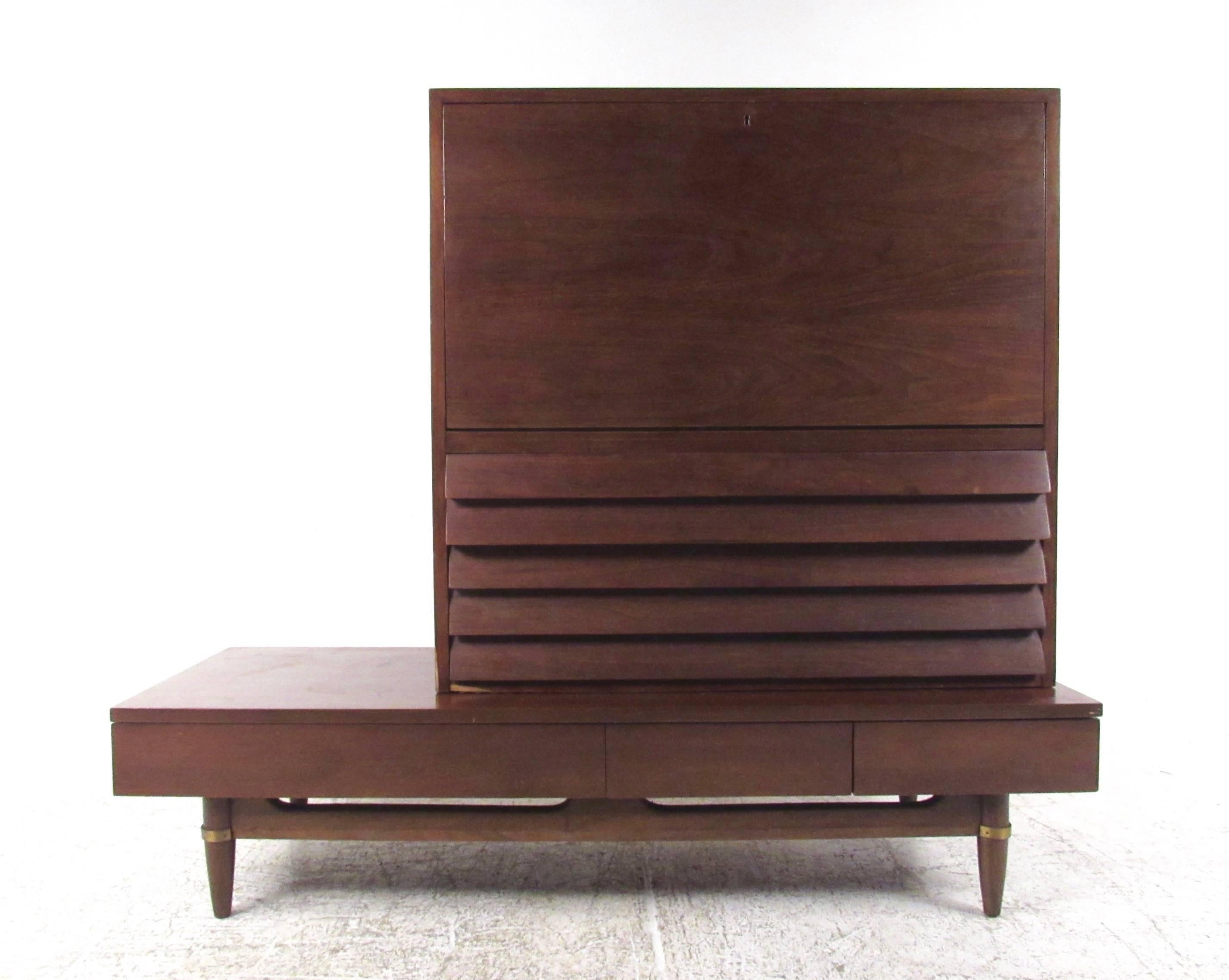 This unique two-piece vintage dresser features a rich walnut finish, louvered front cabinet and unique brass trim. This well made Mid-Century American of Martinsville storage piece features a variety of drawers combined with drop front cabinet for