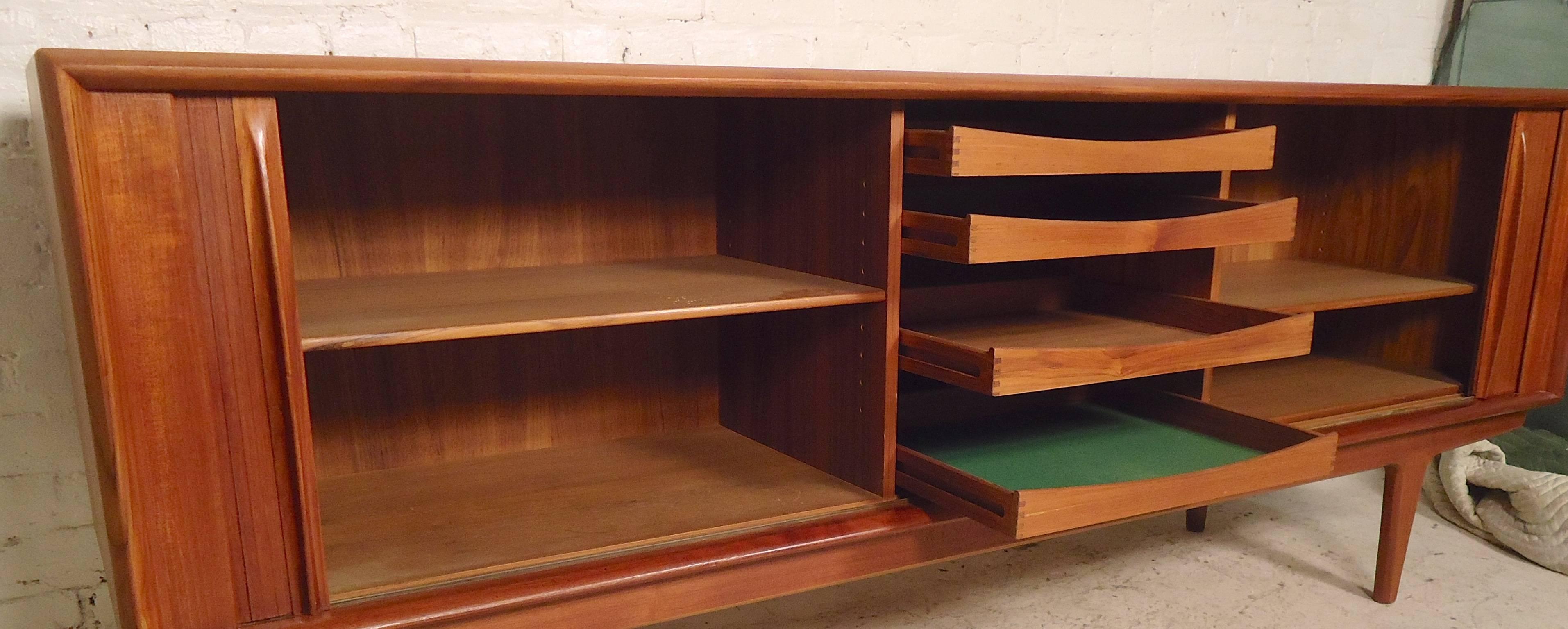 Attractive Mid-Century Modern cabinet with roll-back tambour doors, warm teak grain and tapered legs. Two inside cabinets with adjustable shelves and middle serving drawers. Back is finished.

(Please confirm item location NY or NJ with