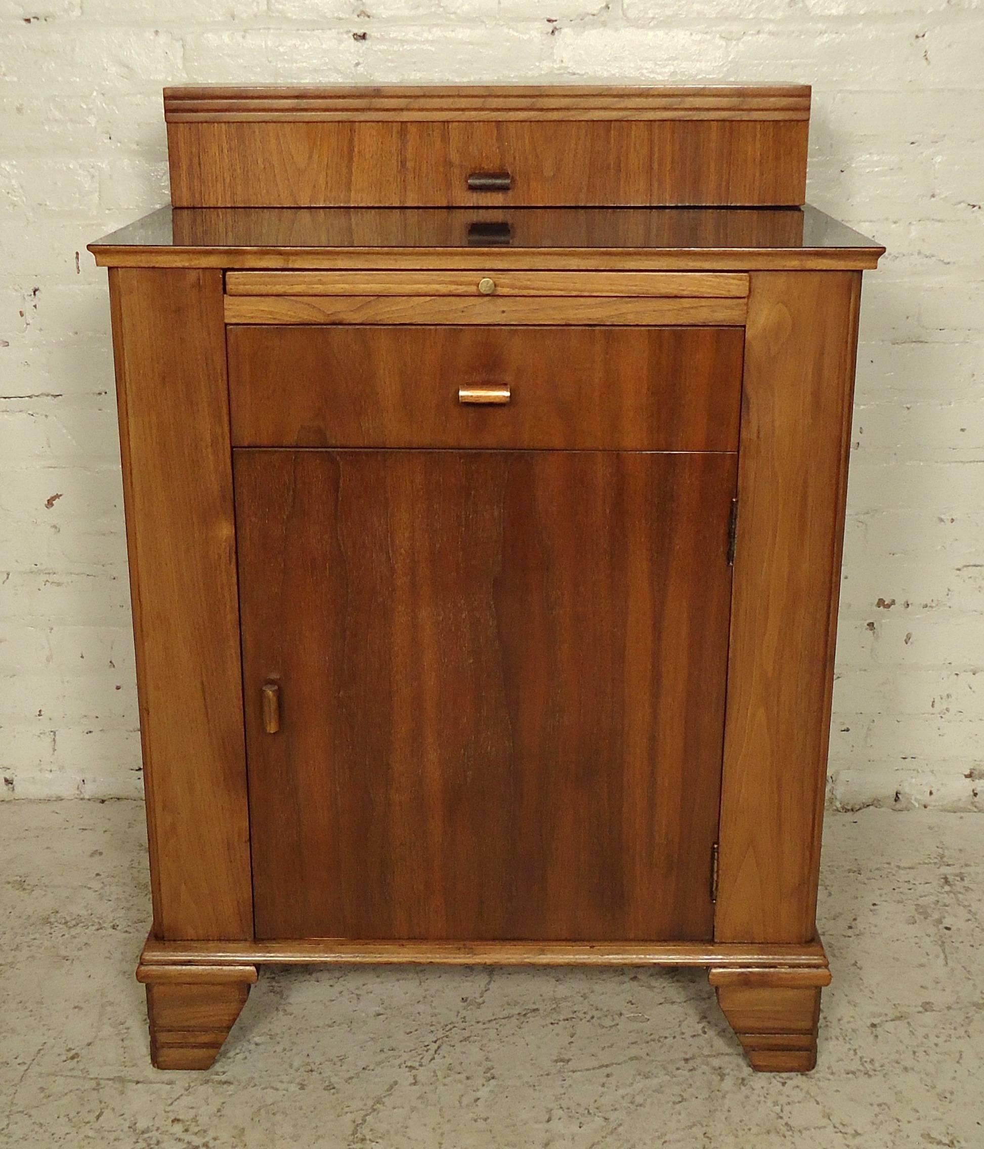 This unique vintage doctors cabinet features a mid-size storage unit, one pull-out shelf over one drawer, and a top compartment above a black Lucite top. This piece has been completely refinished, may contain a few dings along the body and top.