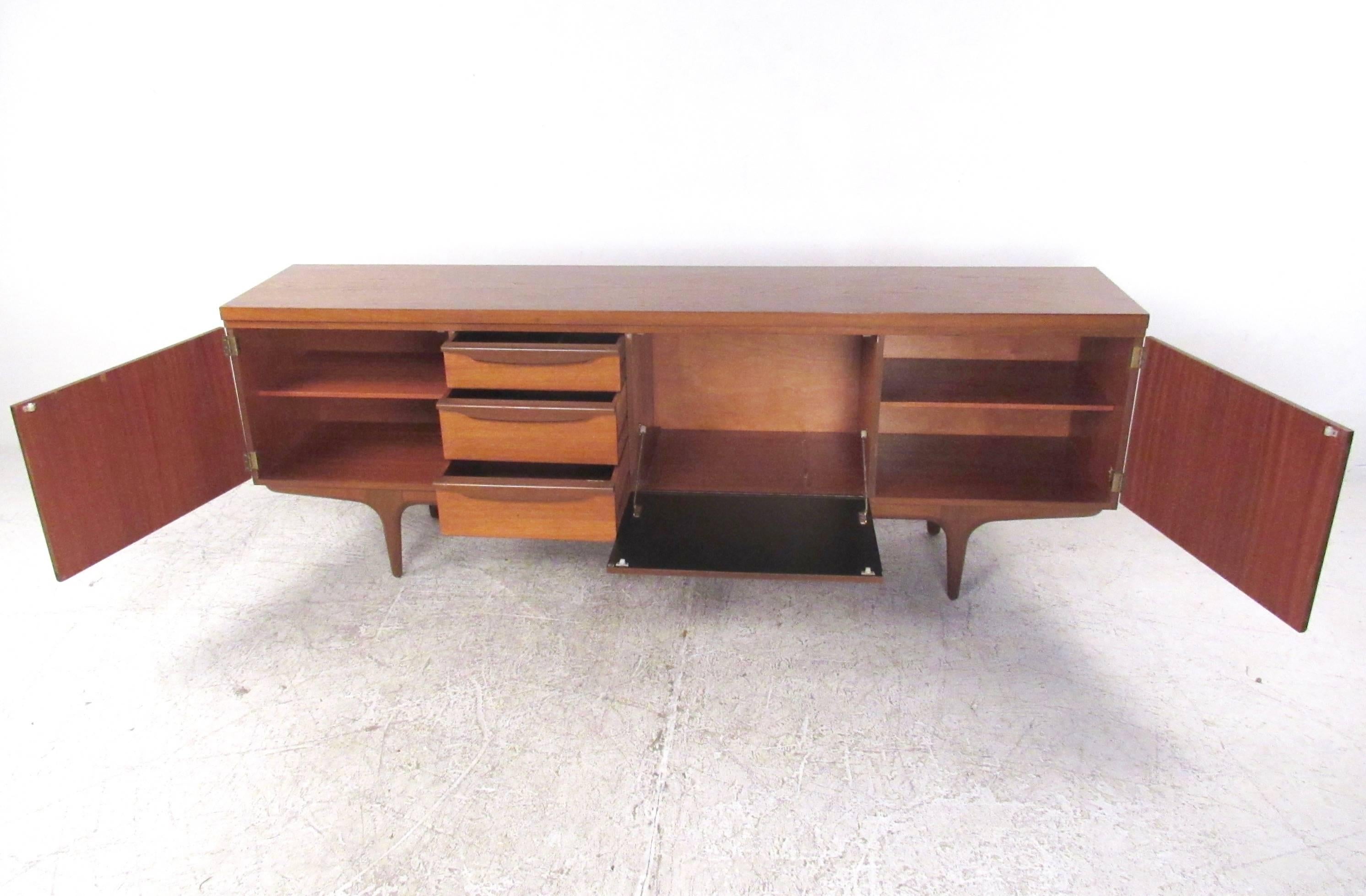 This beautiful vintage teak sideboard features stylish Mid-Century Modern design while offering plenty of storage. Unique carved handles and sturdy tapered legs make this Scandinavian modern server a unique addition to any interior. Please confirm