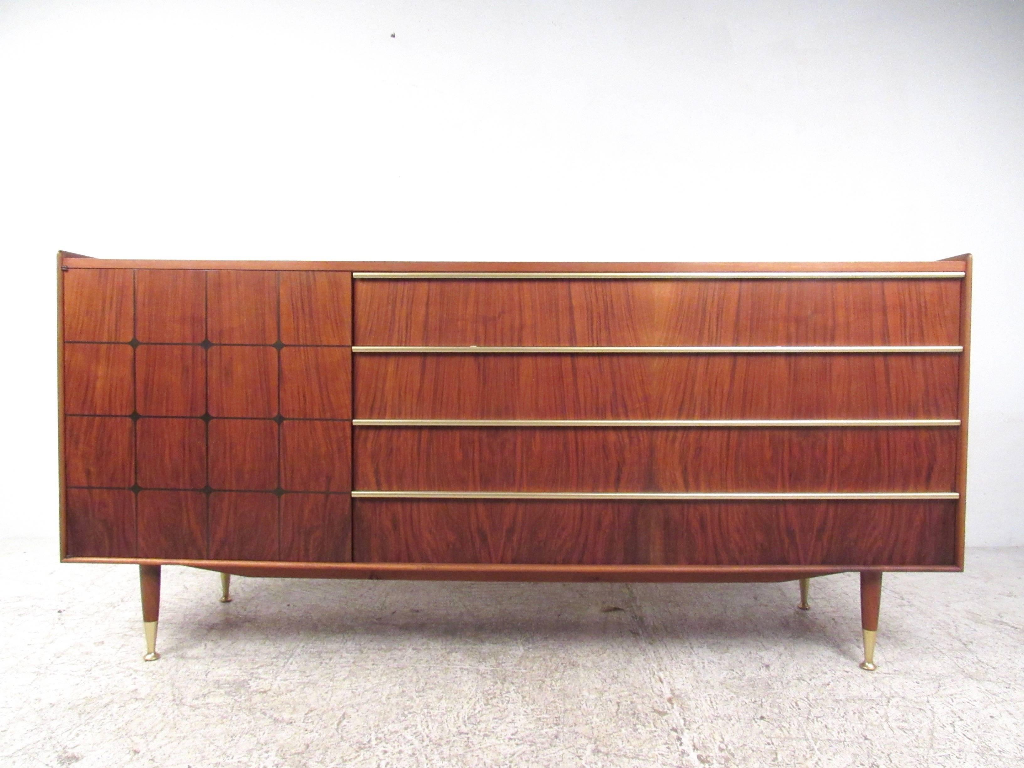 This stunning vintage sideboard features a rich vintage walnut finish with unique brass trim, raised edges, and decorative inlays. Tapered legs and a combination of cabinet and drawer storage further add to the wonderful style of Mid-Century