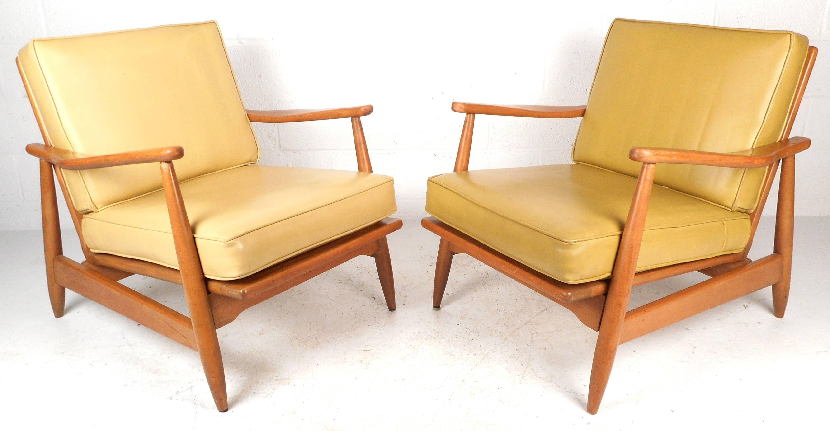 Elegant pair of Mid-Century Modern lounge chairs feature sculpted armrests, tapered legs, spindle backs, and comfortable vinyl cushions. The stylish design and vintage maple finish make them ideal for any interior. Please confirm item location (NY