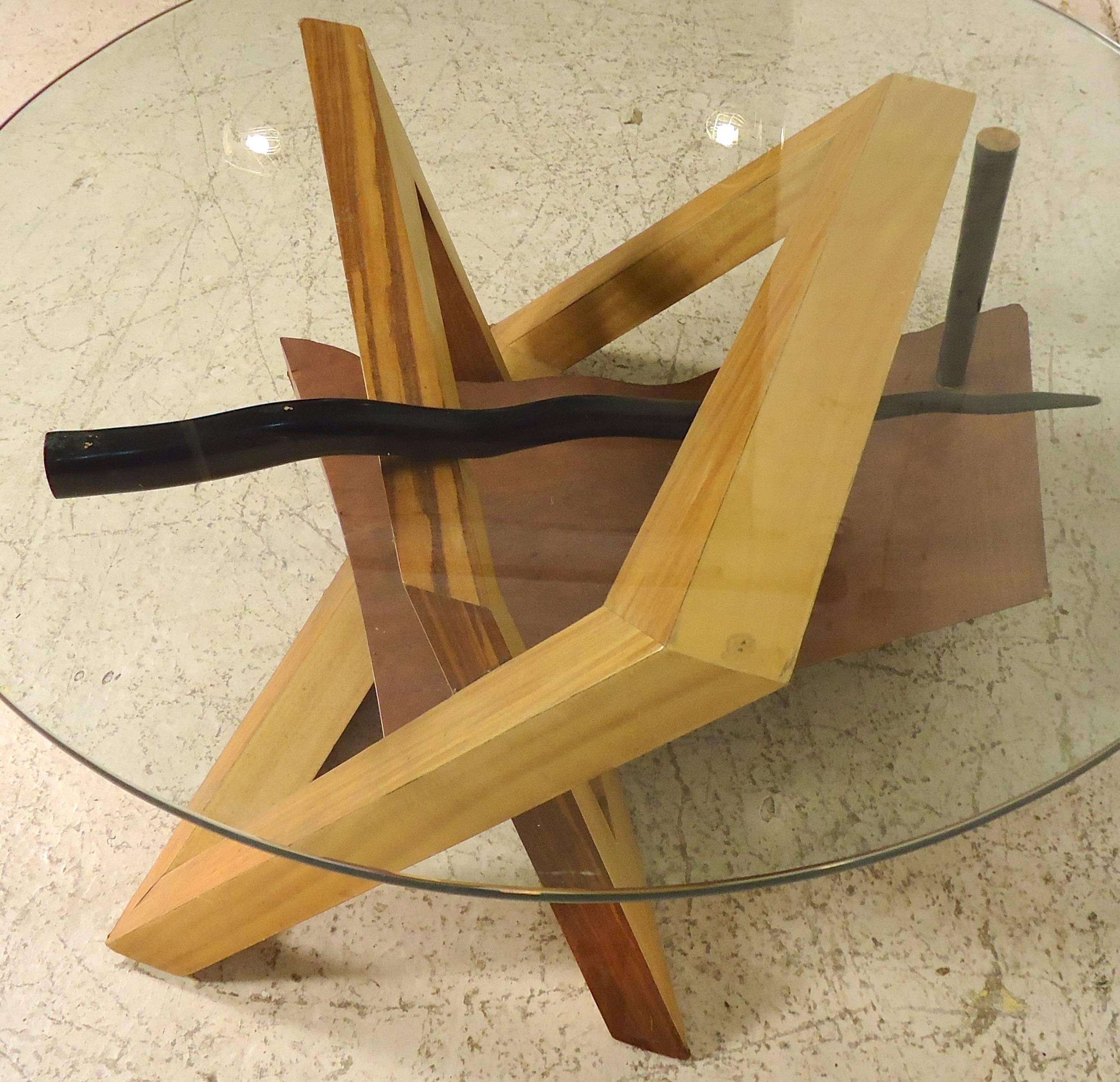 Unusual wood base table with round glass top. The sculpted wood base zig-zags to make sharp angles, and has additional black forms that act as a leg and glass rest. Contemporary style that works well with any modern or Mid-Century motif.

(Please