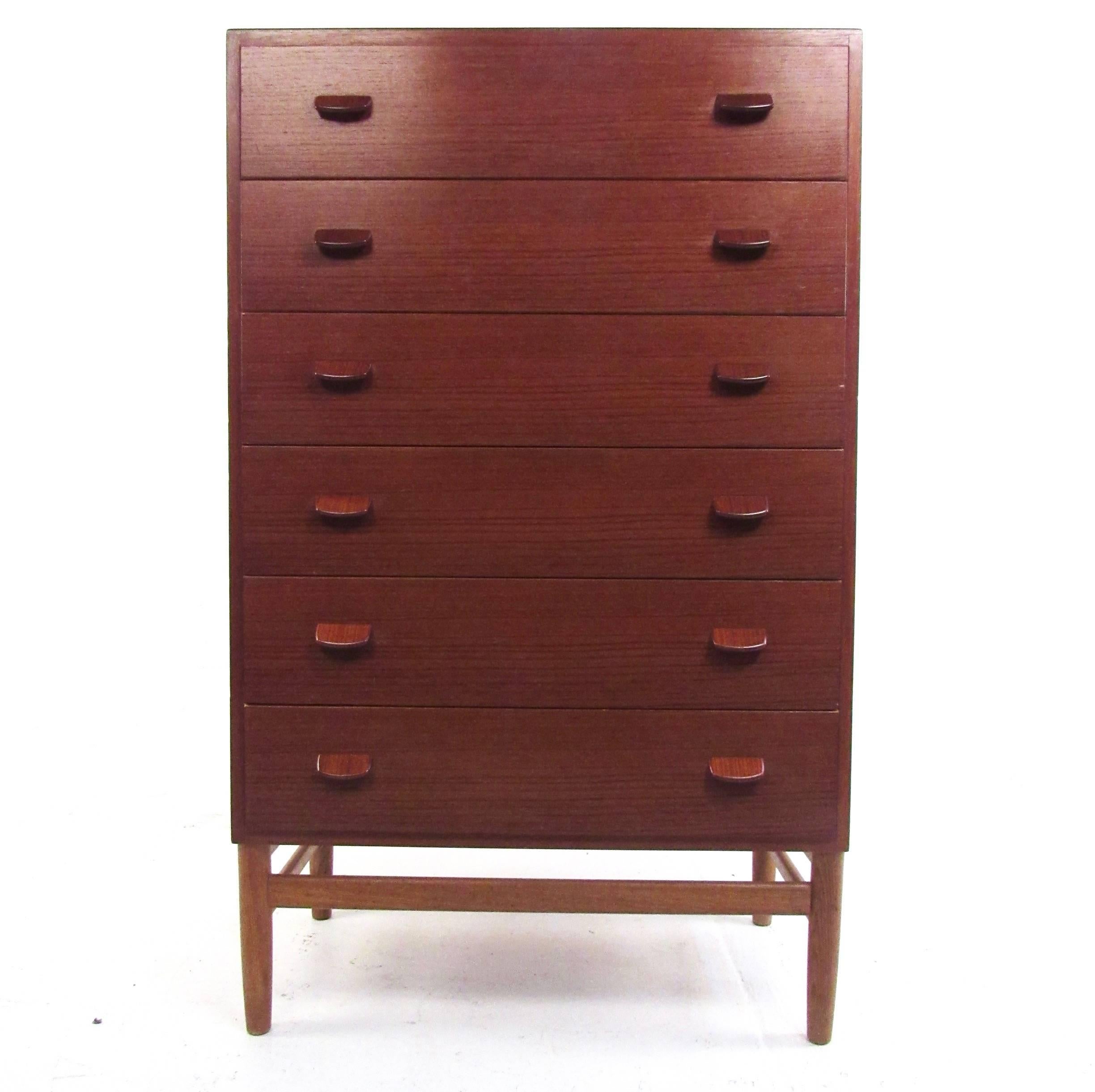 This vintage modern teak dresser features dovetail hardwood drawers with unique carved pulls. Four leg base features tapered stretchers for added stability, while the beautiful Mid-Century teak finish makes a visually impressive addition to any