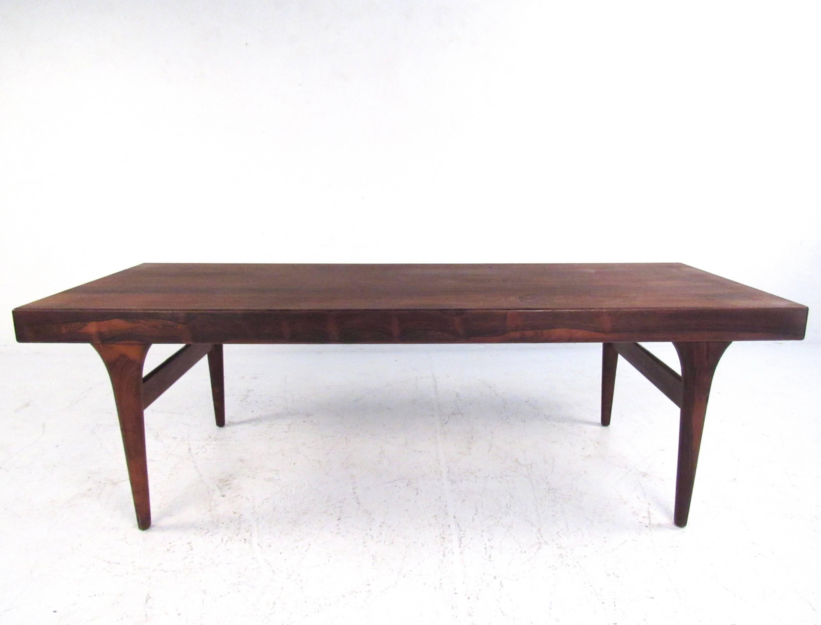 This stunning vintage rosewood coffee table features the unique Mid-Century Modern design of Johannes Andersen. Beautiful rosewood finish is showcased with stylish modern lines, tapered legs, and stretchers for extra support. Each end of the table