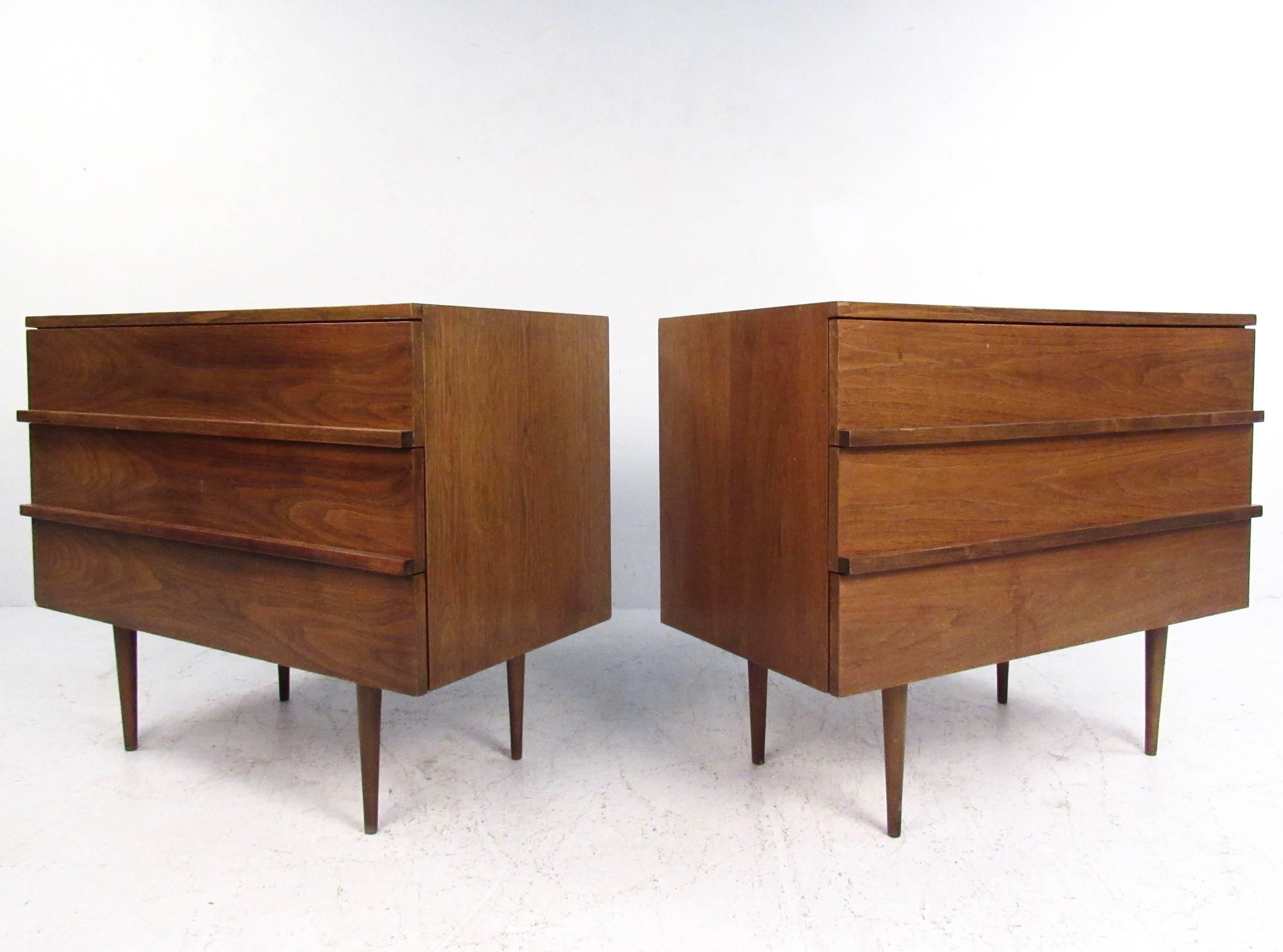 This pair of vintage modern walnut dressers make an excellent addition to any interior in need of stylish storage. Thin and tall tapered legs offset the wide design and robust walnut finish. Carved drawer pulls and plenty of storage space make these