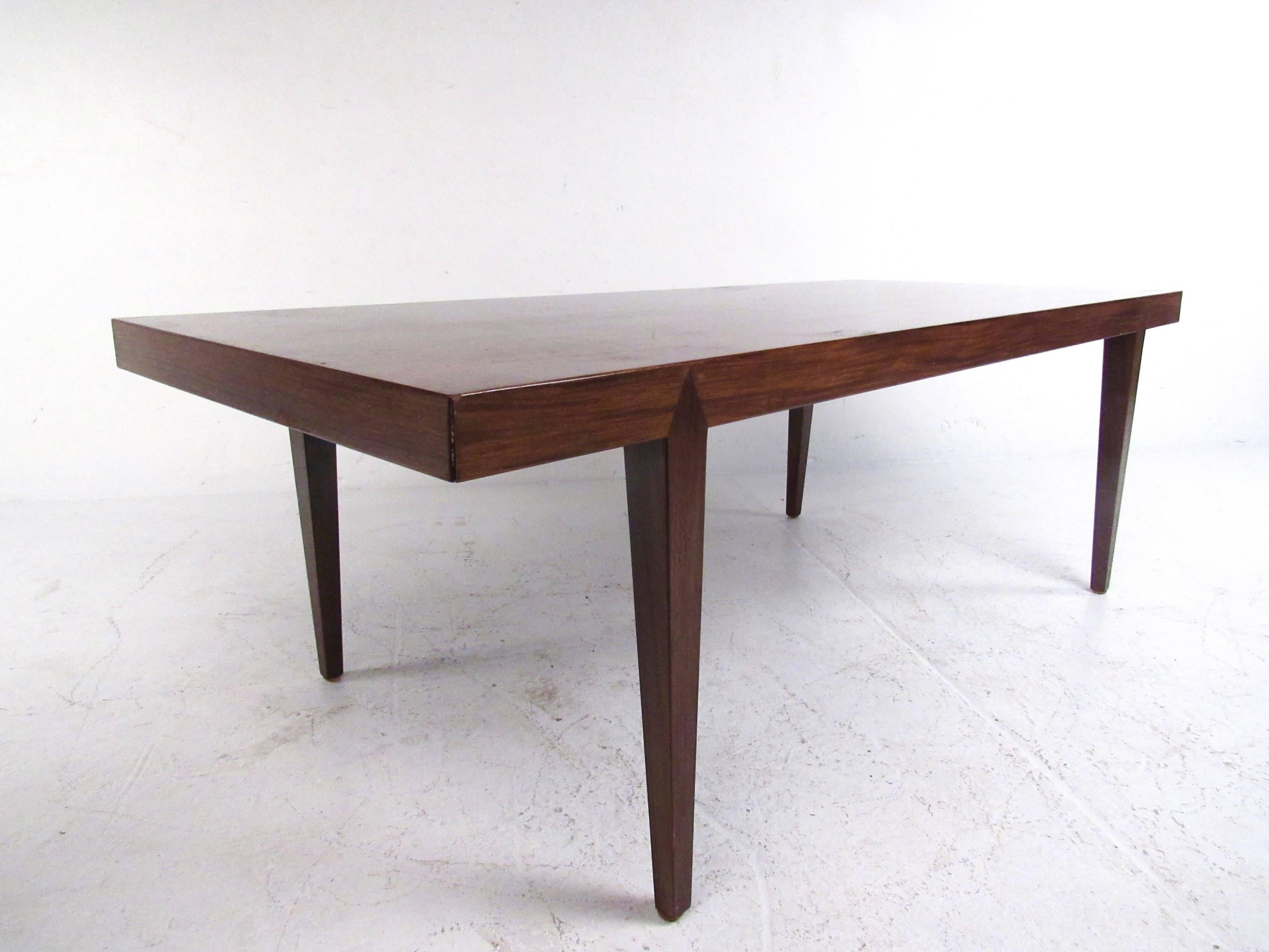 Cette table basse vintage unique en bois de rose présente de grands pieds effilés et minces avec une construction articulée unique. La magnifique finition vintage ajoute au charme Mid-Century de cette table de cocktail qui constitue une pièce