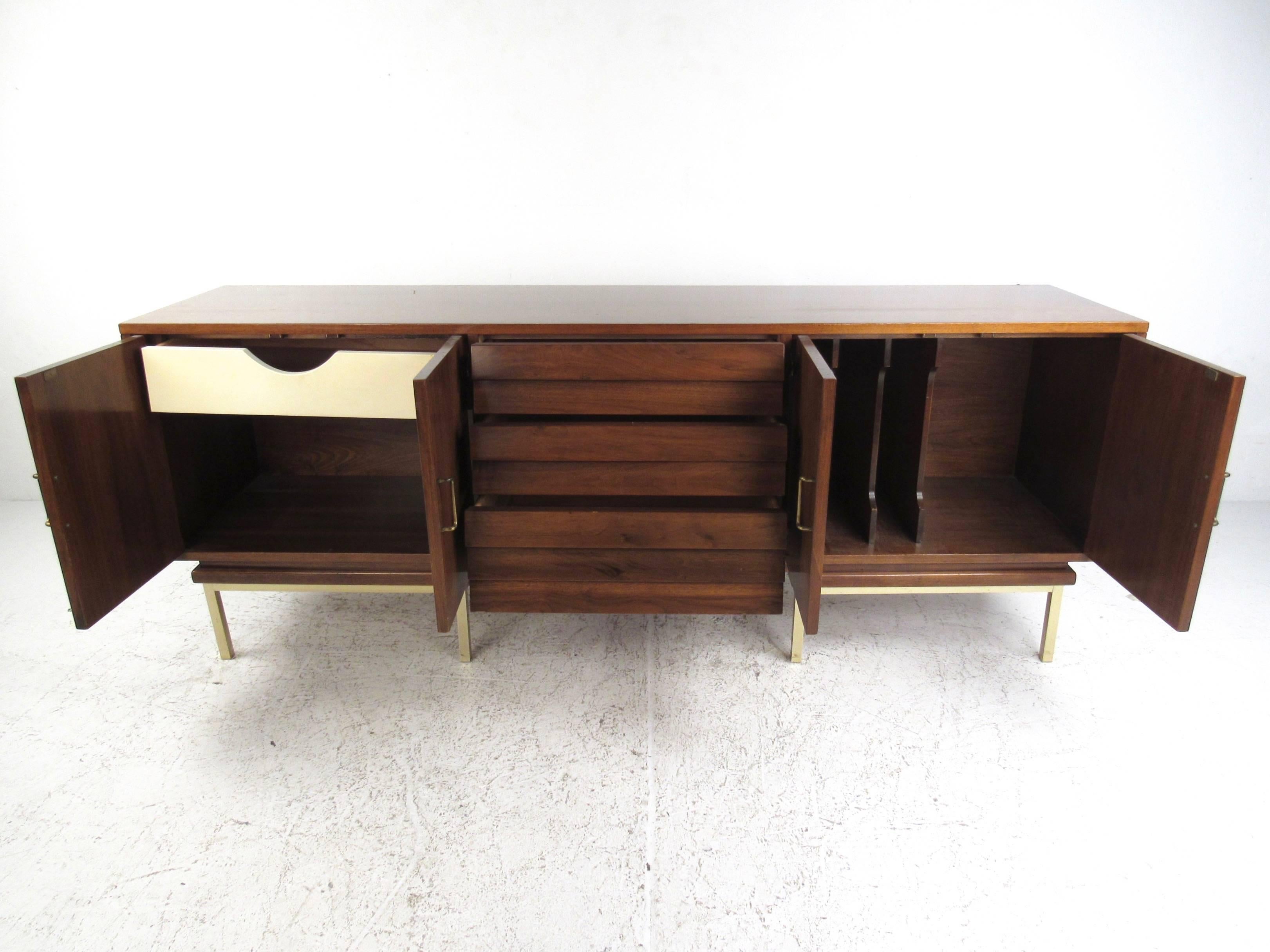 This large scale American walnut sideboard features louvered drawer fronts, brass finish trim and a combination of storage options. Three center drawers are paired with Dual side cabinets for concealed storage. Brass handles and rich vintage walnut