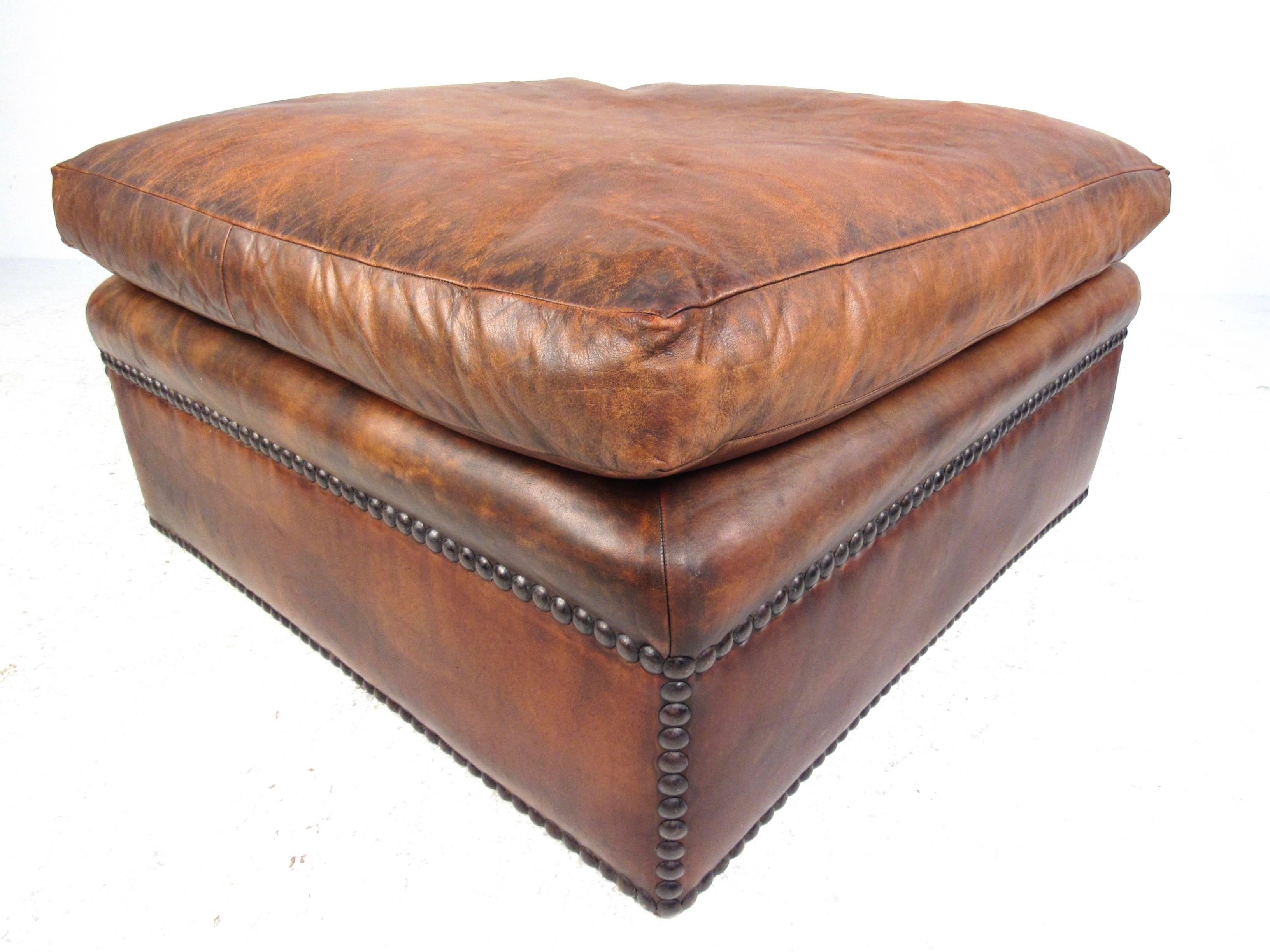 This wonderful ottoman features rich leather upholstery with brass studded trim. Wonderfully aged with light patina to studs and leather, this large ottoman is a comfortable and stylish addition to any seating arrangement. Please confirm item