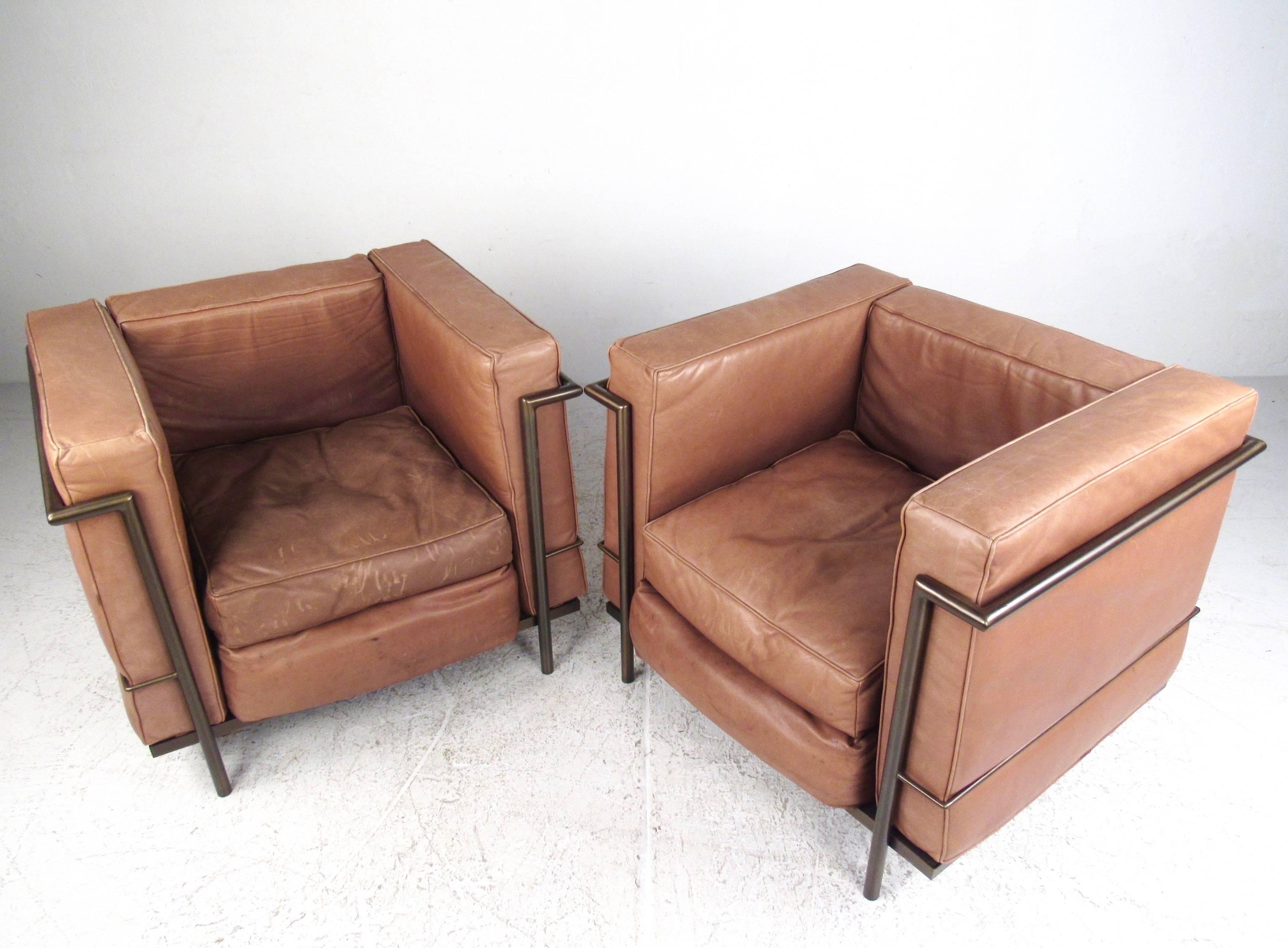 This stylish pair of vintage leather club chairs feature Le Corbusier LC2 style design, including five cushion seats, with polished brass finish metal frame. Wonderful mix of modern aesthetics and vintage style, the lightly worn overstuffed leather