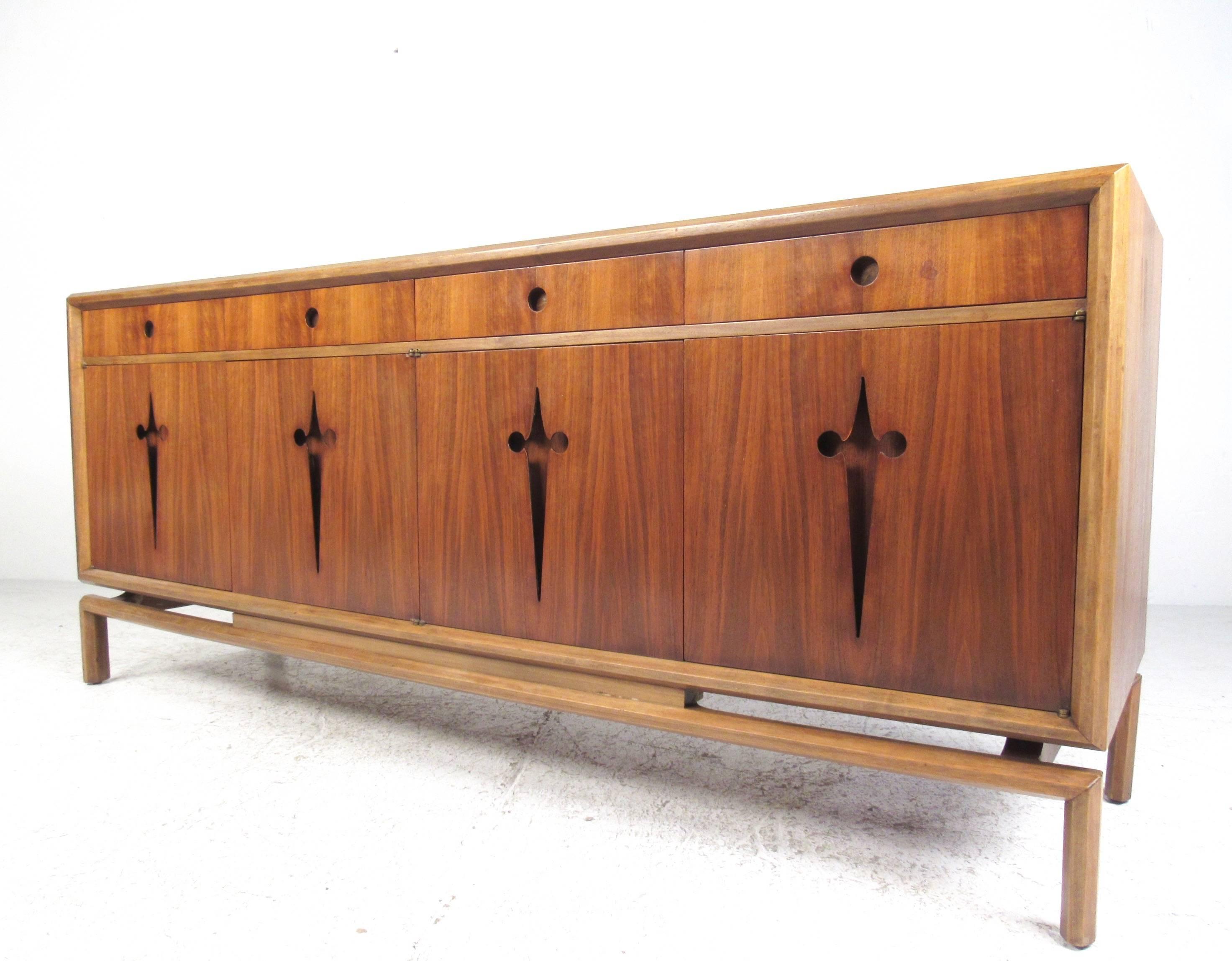 This stunning Mid-Century Modern storage credenza by Edmond Spence features six internal drawers beneath a set of four shallow silver drawers. Beautiful vintage finish is accented by cutaway fleur-de-lis details, while the top drawers feature unique