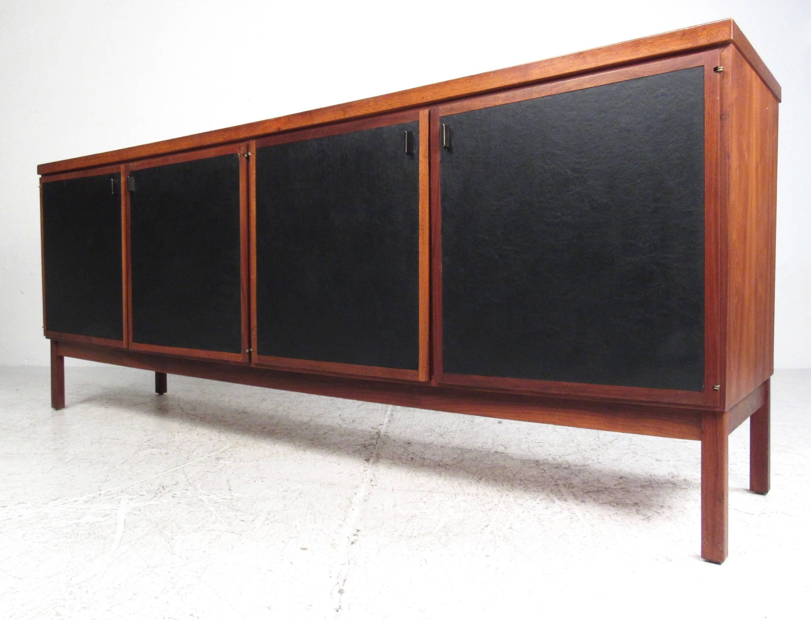This stunning storage piece features faux leather door fronts and quality teak and walnut construction. Based on a similar design by John Stuart, this Mid-Century Modern piece offers plenty of room for storage and organization in any setting. Please