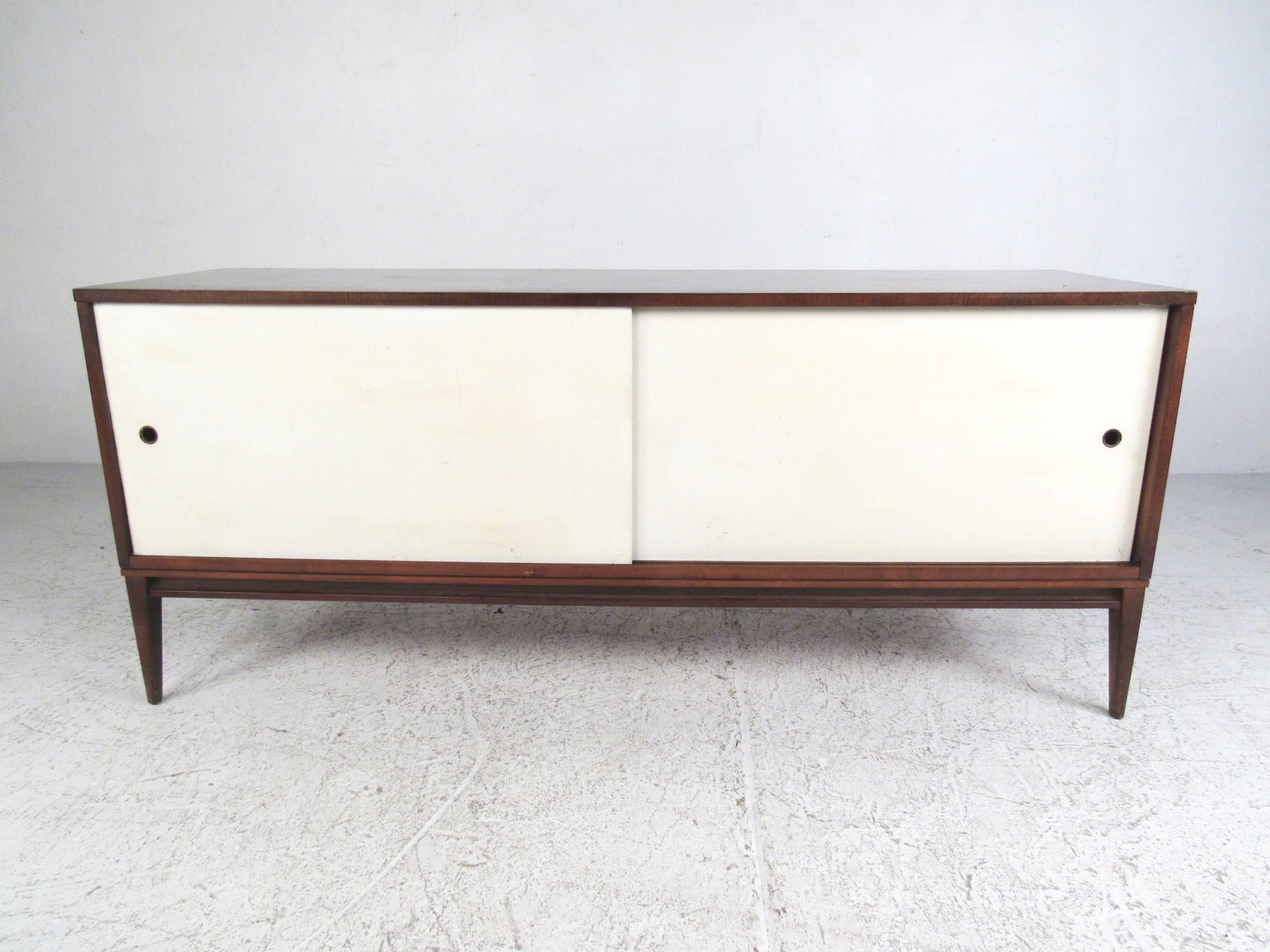 This vintage modern sliding door credenza features the unique mid-century construction of Paul McCobb and features tapered legs, simple lines, and cloth lines doors. Spacious interior cabinet space makes this ideal for home or office, and a great