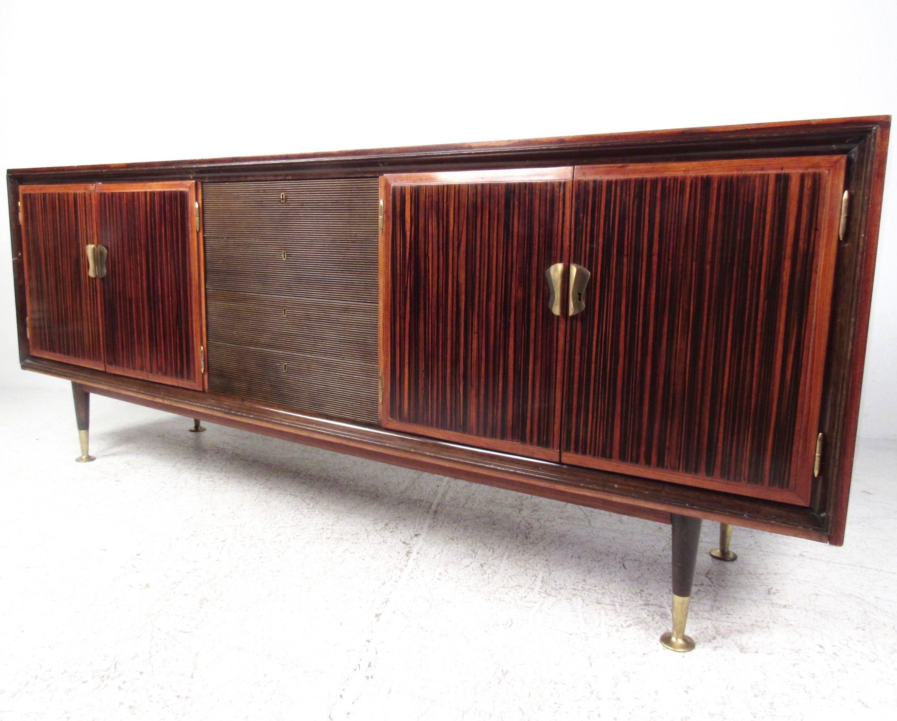 This large-scale Mid-Century sideboard features rich Italian rosewood construction, wide grain cabinet front doors, and unique brass finish trim. Exquisite Osvaldo Borsani style design, the spacious cabinet space is complimented by a set of center