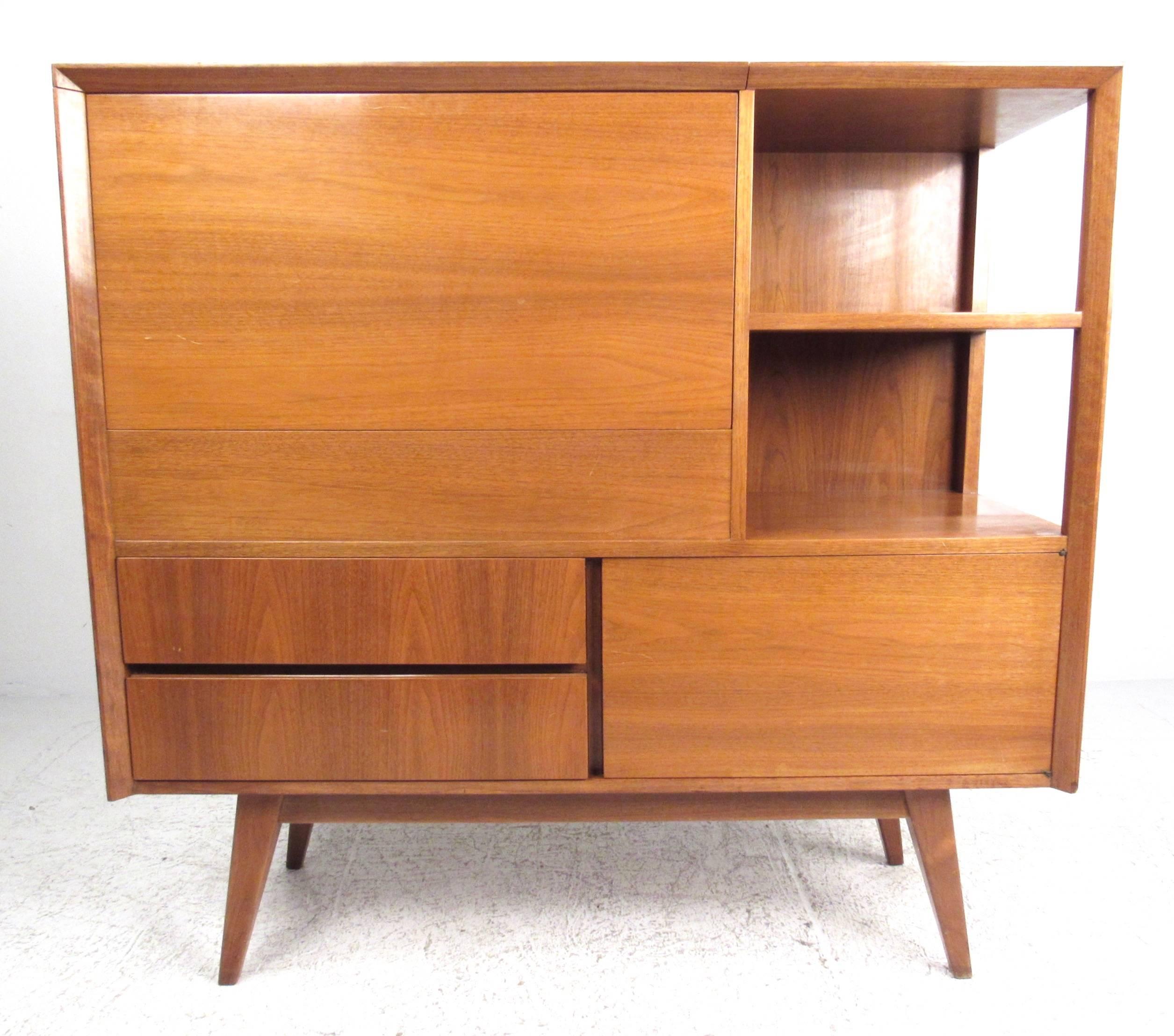 This unique vintage bar cabinet features a beautiful Mid-Century array of storage options complete with drop front laminate bar with mirrored back and glass shelf. Sculpted tapered legs, shelf display, and drawer or cabinet storage add to the