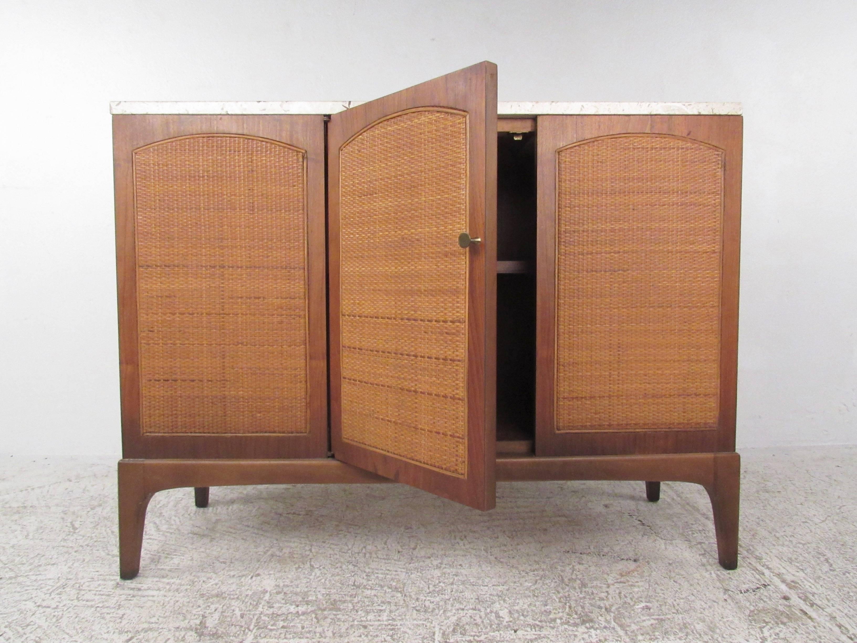 This stylish vintage credenza features three panel cane front doors with tapered walnut legs and brass pull. Mid-Century marble top adds to the elegant charm of this unique storage cabinet. Spacious interior shelf storage makes this a versatile