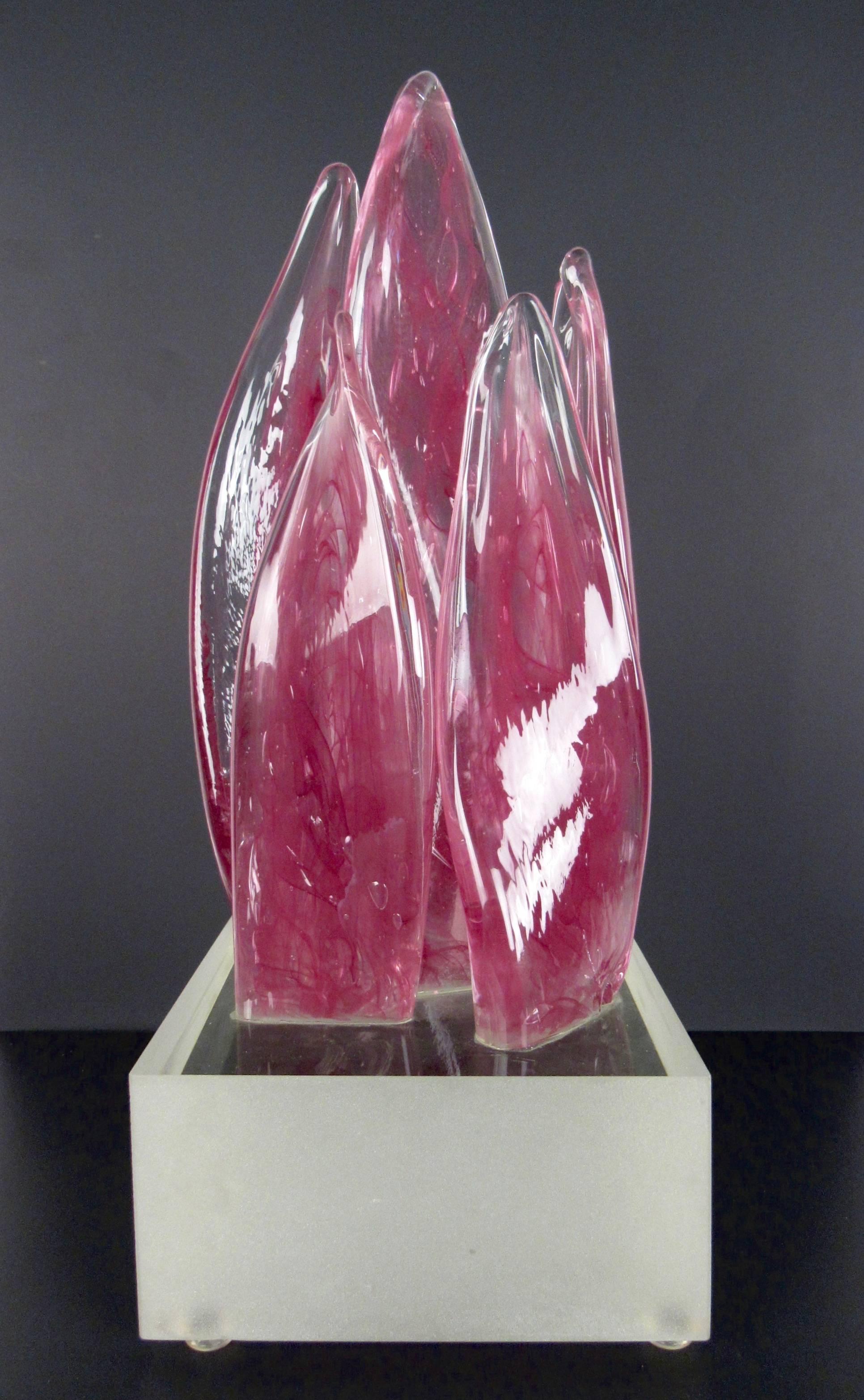 This unique sculpted art glass piece features a unique depiction of colored glass in a free flowing torch flame style design. Mounted carefully on a glass base this elegant modern art sculpture makes a unique addition to home or office decor. Please
