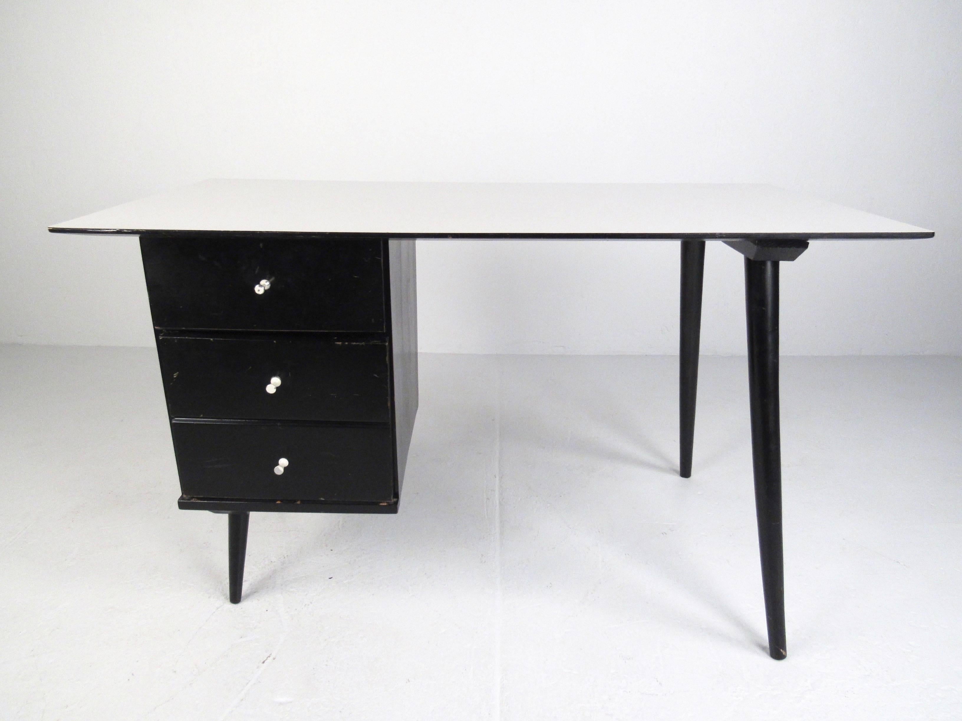 This vintage modern pedestal desk features the iconic mid-century design of Paul McCobb. Single sided writing desk offers two drawers for storage and organization and a spacious formica-style top for work. Slender tapered legs and unique McCobb
