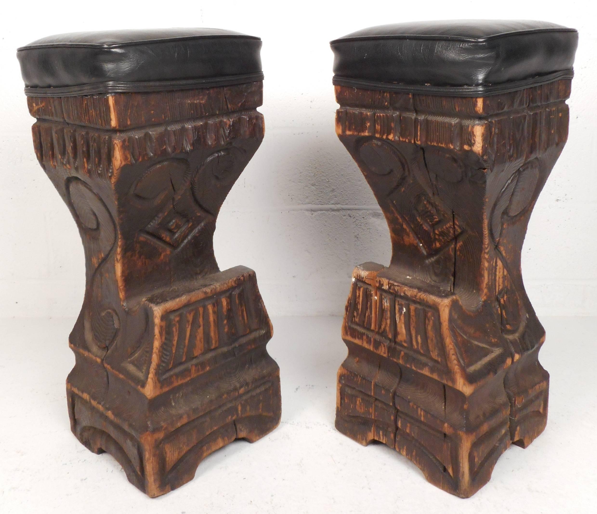 Stylish pair of vintage modern tiki bar stools feature teakwood bases with unique detailed south pacific primitive style carvings. The comfortable black vinyl seat offers comfort and style in any modern interior. Please confirm item location (NY or