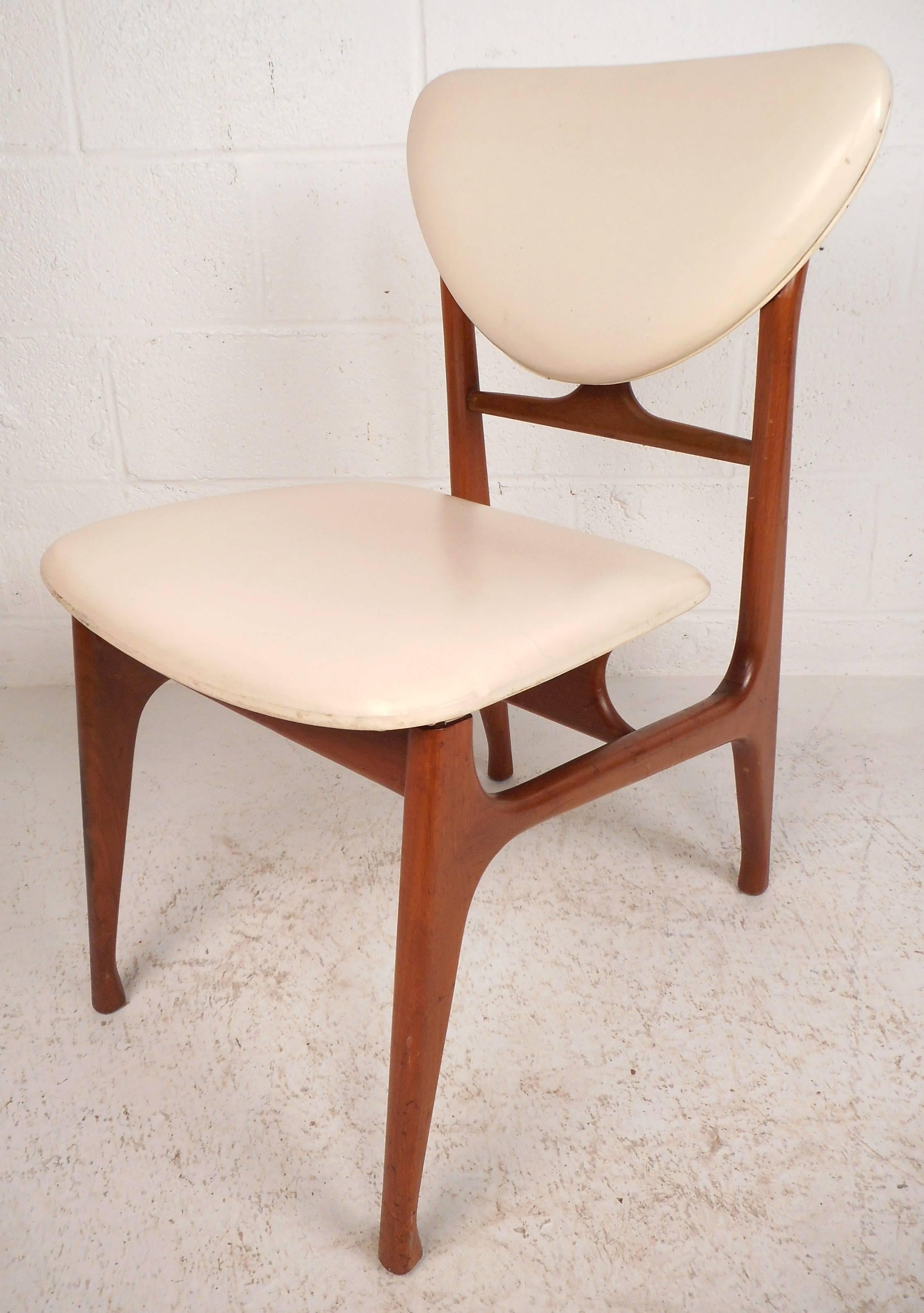 Stunning set of four Mid-Century Modern dining chairs feature a vintage teak finish and a unique sculpted frame. The stylish floating seat and shapely backrest provide optimal comfort. The beautiful white vinyl upholstery is sure to add style to any