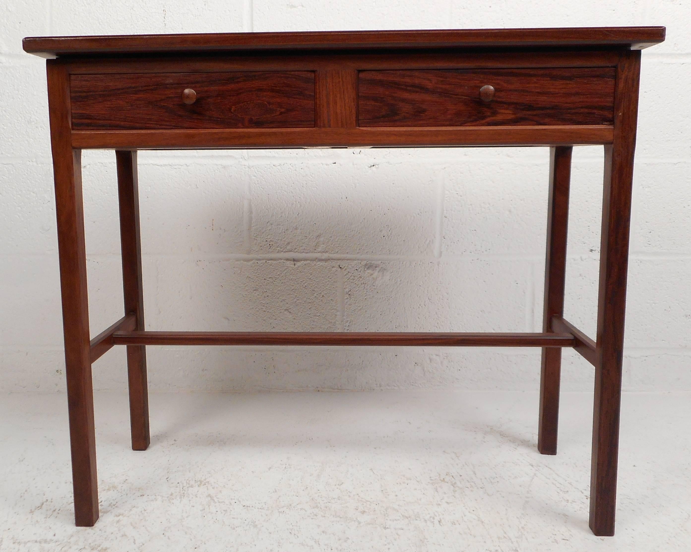 Lovely vintage modern small console table features two drawers with unique round pulls. Beautiful vintage rosewood finish with three stretchers between four sturdy legs ensure style and sturdiness. Sleek finished rosewood back makes it the perfect