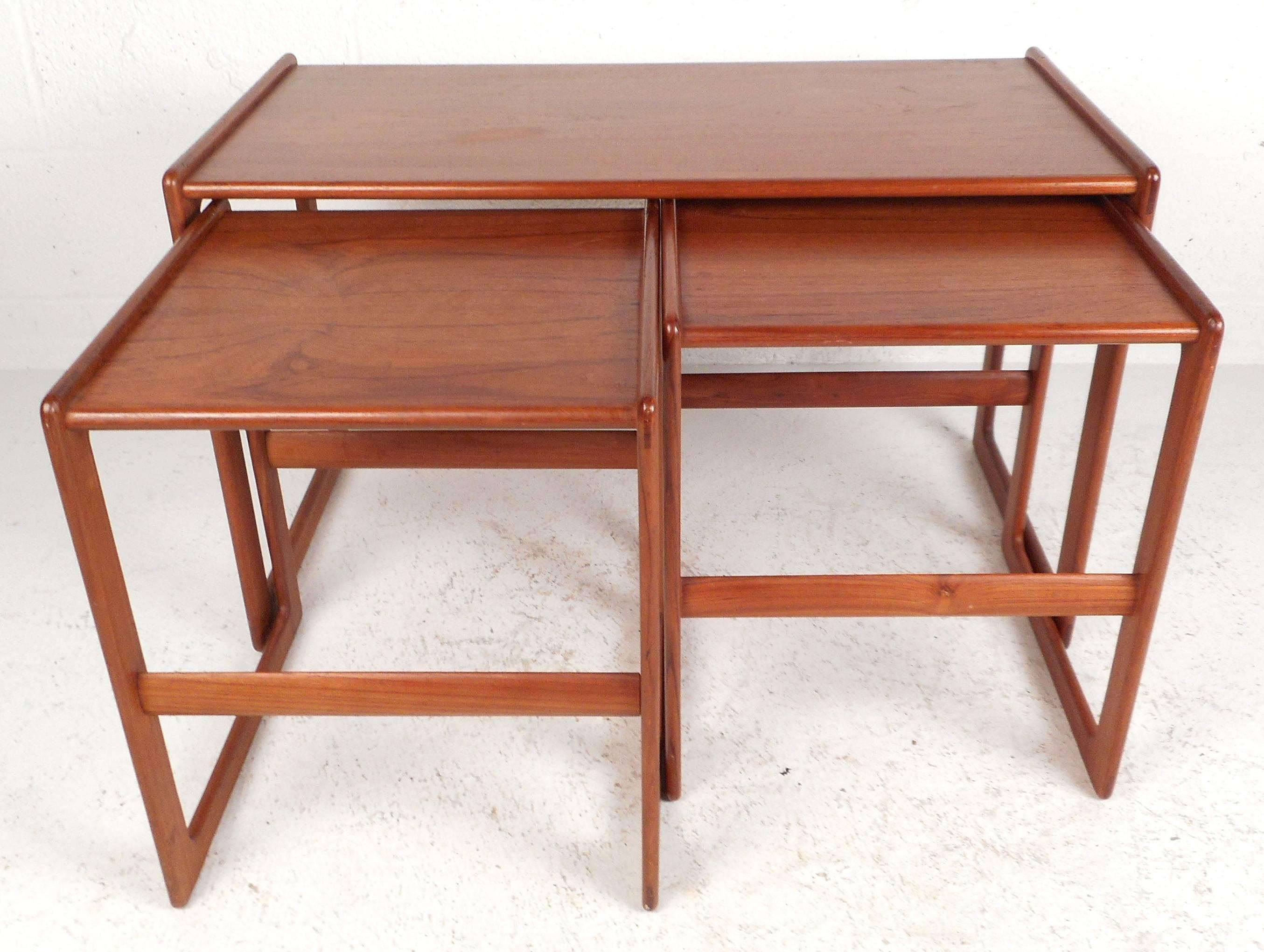 Stunning set of three Mid-Century Modern stacking tables feature beautiful teakwood grain and unique sled legs. The stylish design allows the two smaller tables to nestle comfortably underneath the larger one offering convenient storage. Beautiful