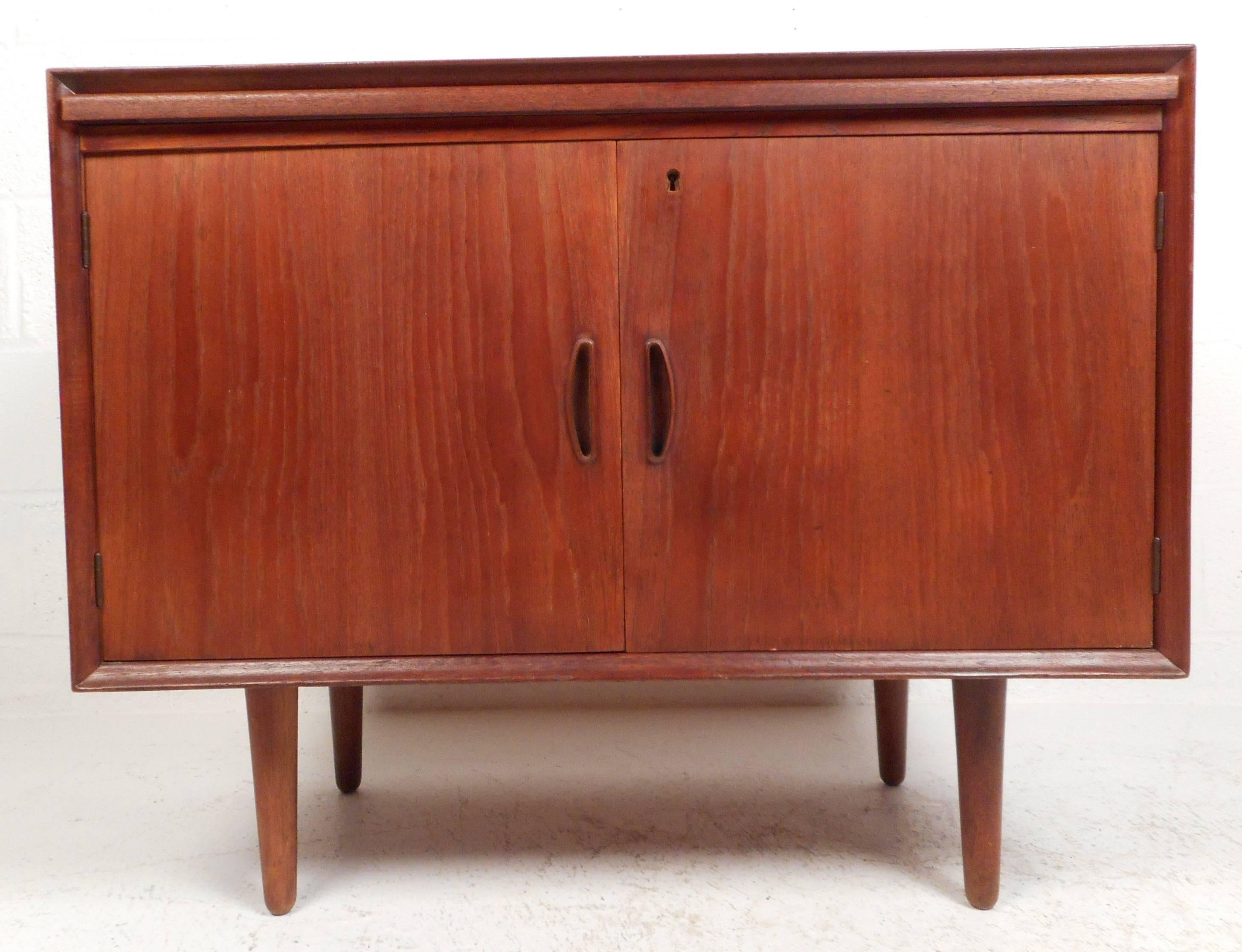 Gorgeous vintage modern small two-door server features unique carved pulls and a pullout Formica top tray. Sleek design with a vintage teak finish and four tapered legs. Stamped 