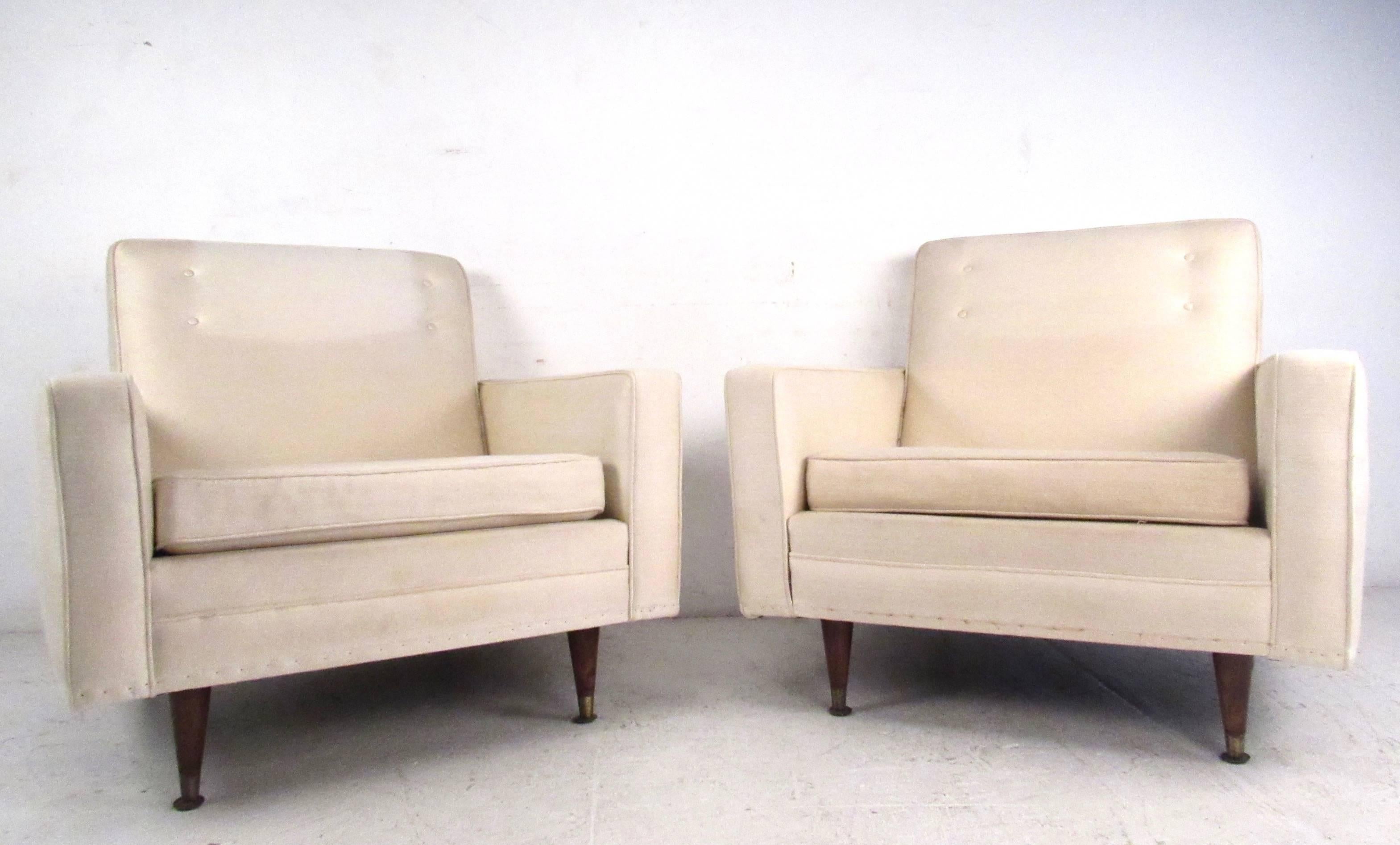 This pair of Mid-Century Modern lounge chairs feature the simplistic modern style of the 1960s and 1970s, with spacious comfortable seats, tapered legs, and brass feet. Button tufted seat backs and ample padding add to the appeal of this vintage