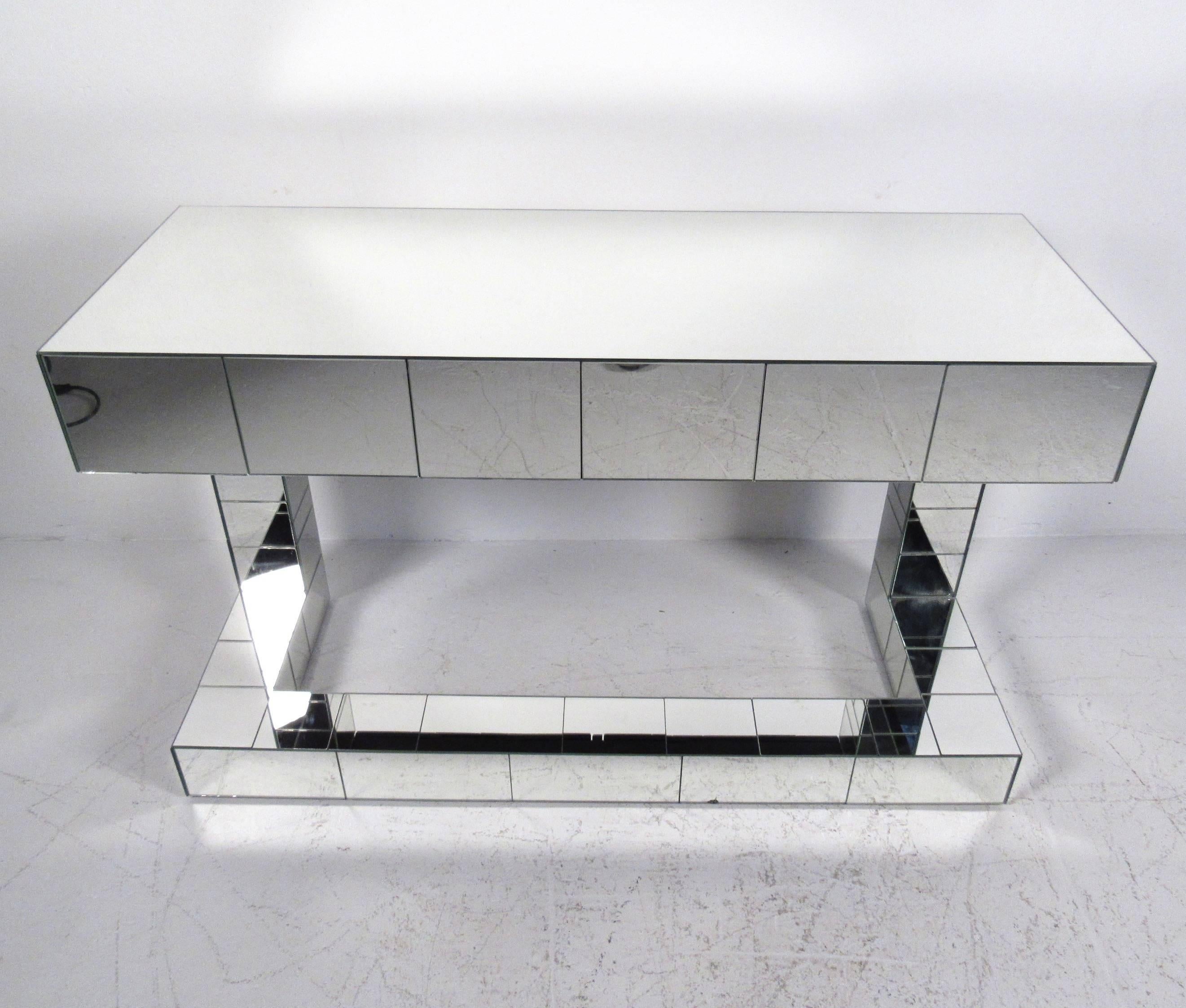 This unique mirrored console table does double duty as a console table and occasional writing table. Two drawers offer concealed storage while the mirrored panel Paul Evans style finish makes a stylish modern addition to any interior decor. Please