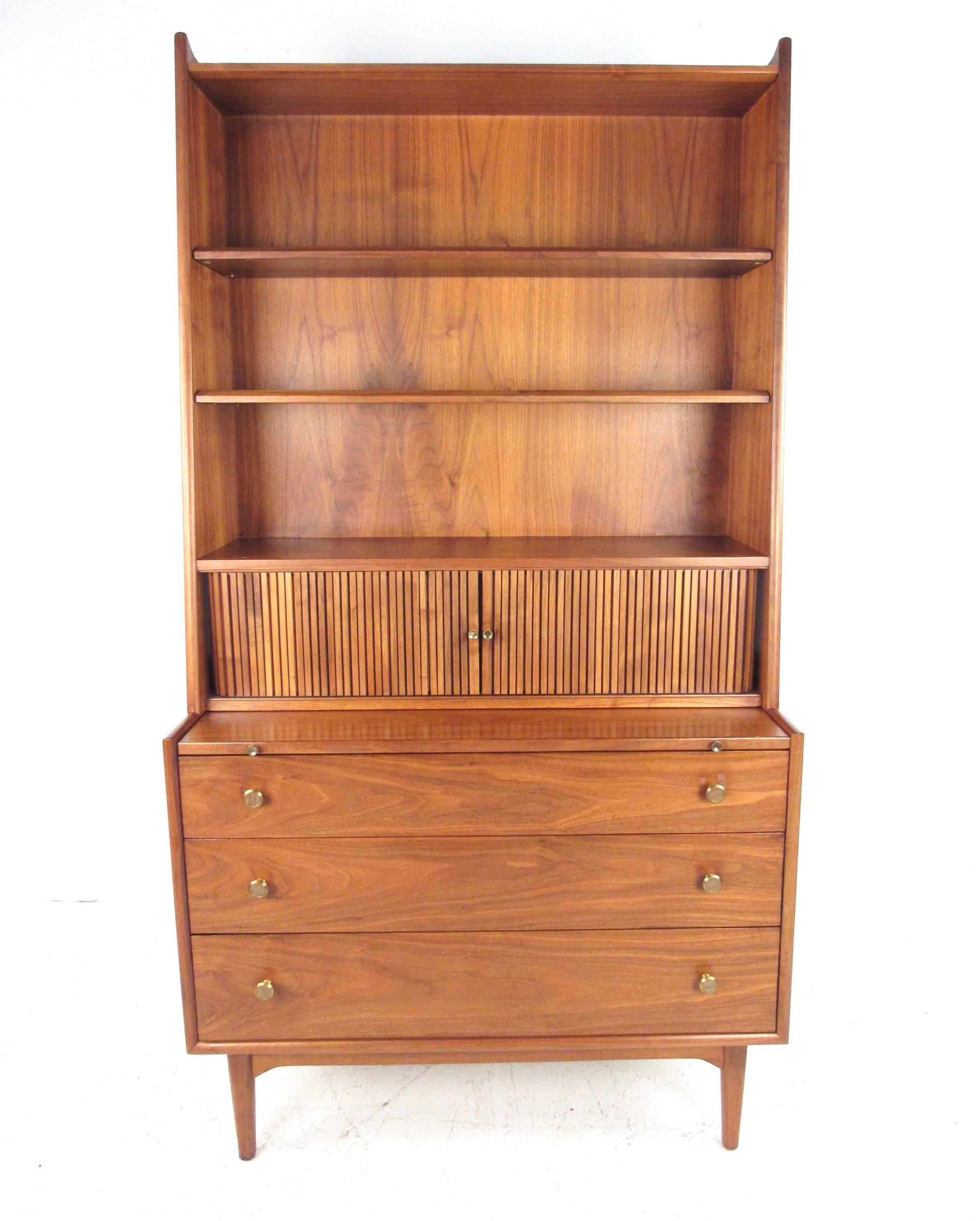 This vintage American walnut bookcase features Drexel Furniture design with beautiful hardwood finish. Unique brass trim on handles add to the Mid-Century style, while tambour desktop cabinet adds room for organization and storage about pull-out