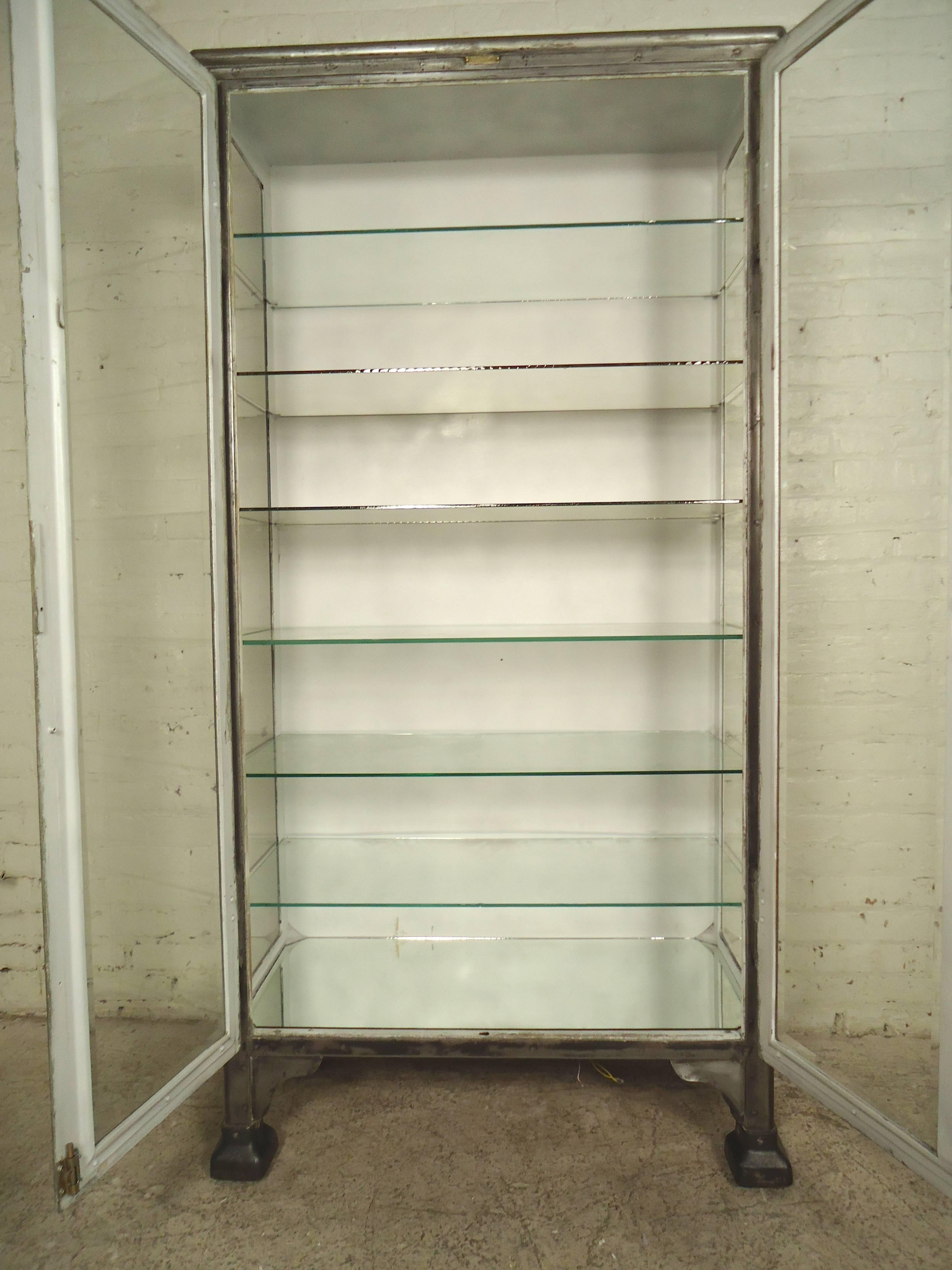This restored metal cabinet has been stripped down and given a unique bare metal style finish. Complete with mirrored bottom, six thick removable glass shelves, locking mechanisms, and rolling casters.
This is a heavy unit that features three glass