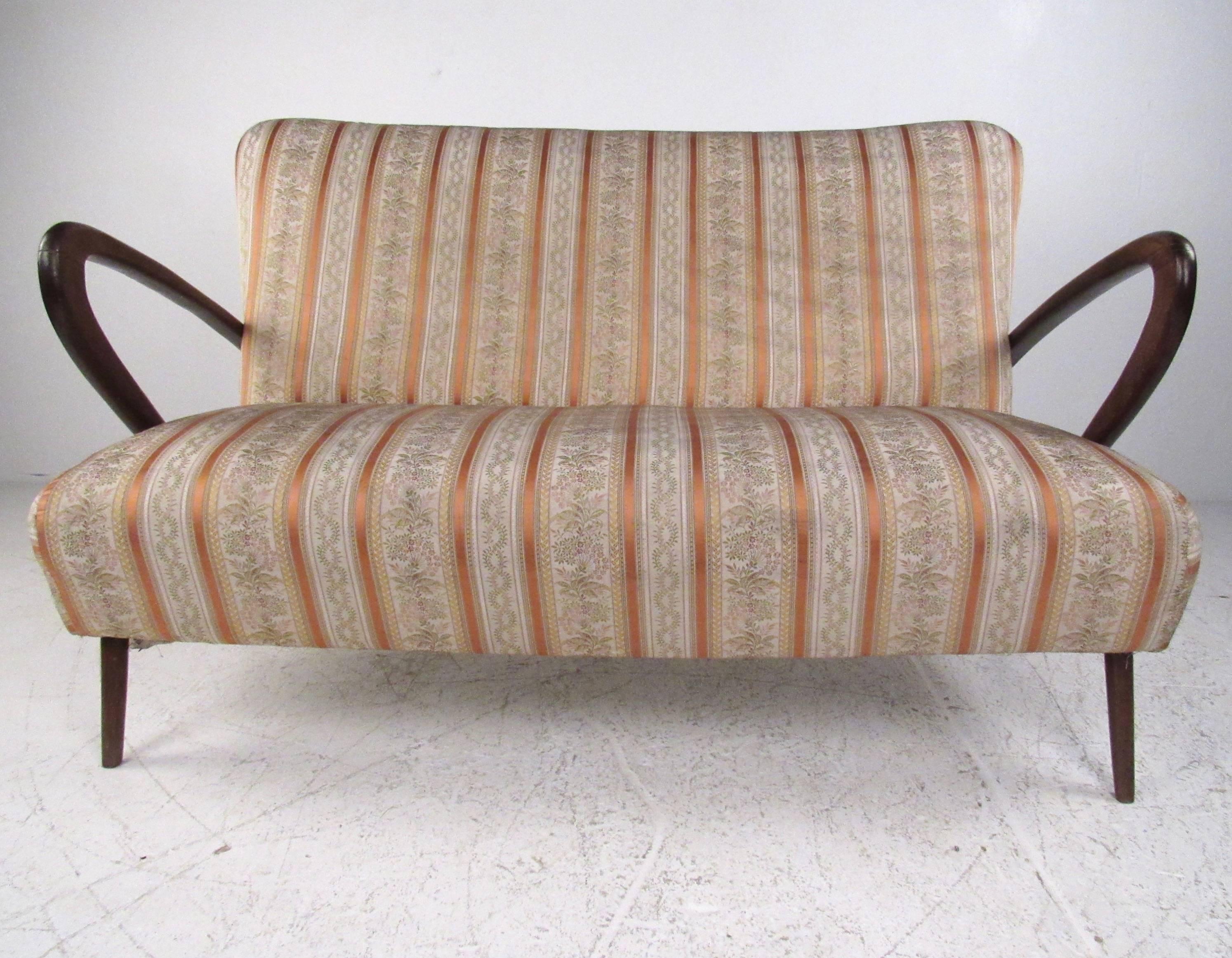 This stunning two seat settee features sculpted hardwood arms with sleek and delicate legs. Unique vintage fabric adds to the mid-century appeal of this elegant Italian love seat. Matching arm chairs available, please confirm item location (NY or