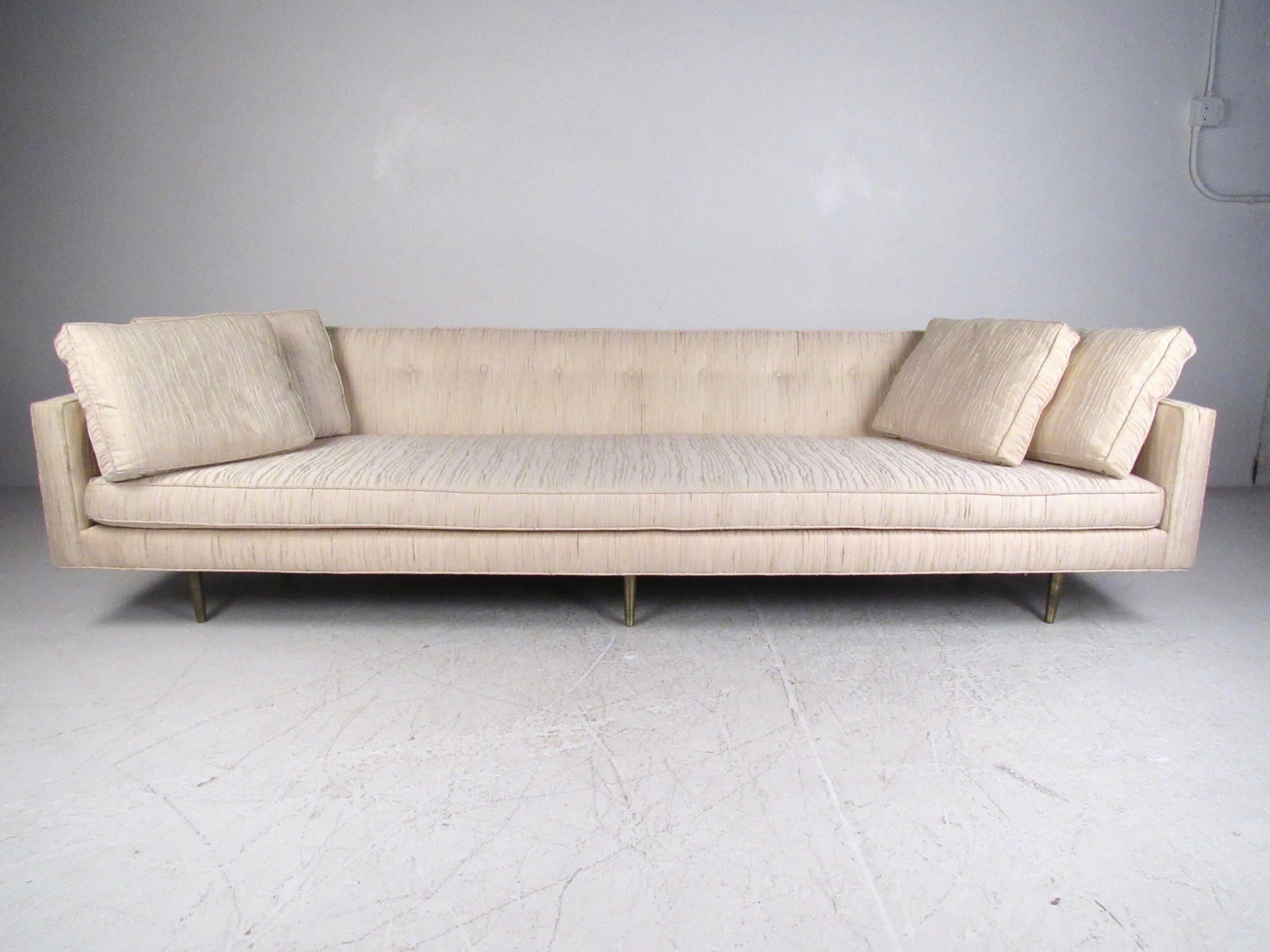 This large, stylish, Mid-Century Modern sofa by Edward Wormley for Dunbar features tufted vintage fabric, unique cutaway curved back, and tapered brass legs. Impressive in size and style, this long vintage sofa makes a beautiful addition to any
