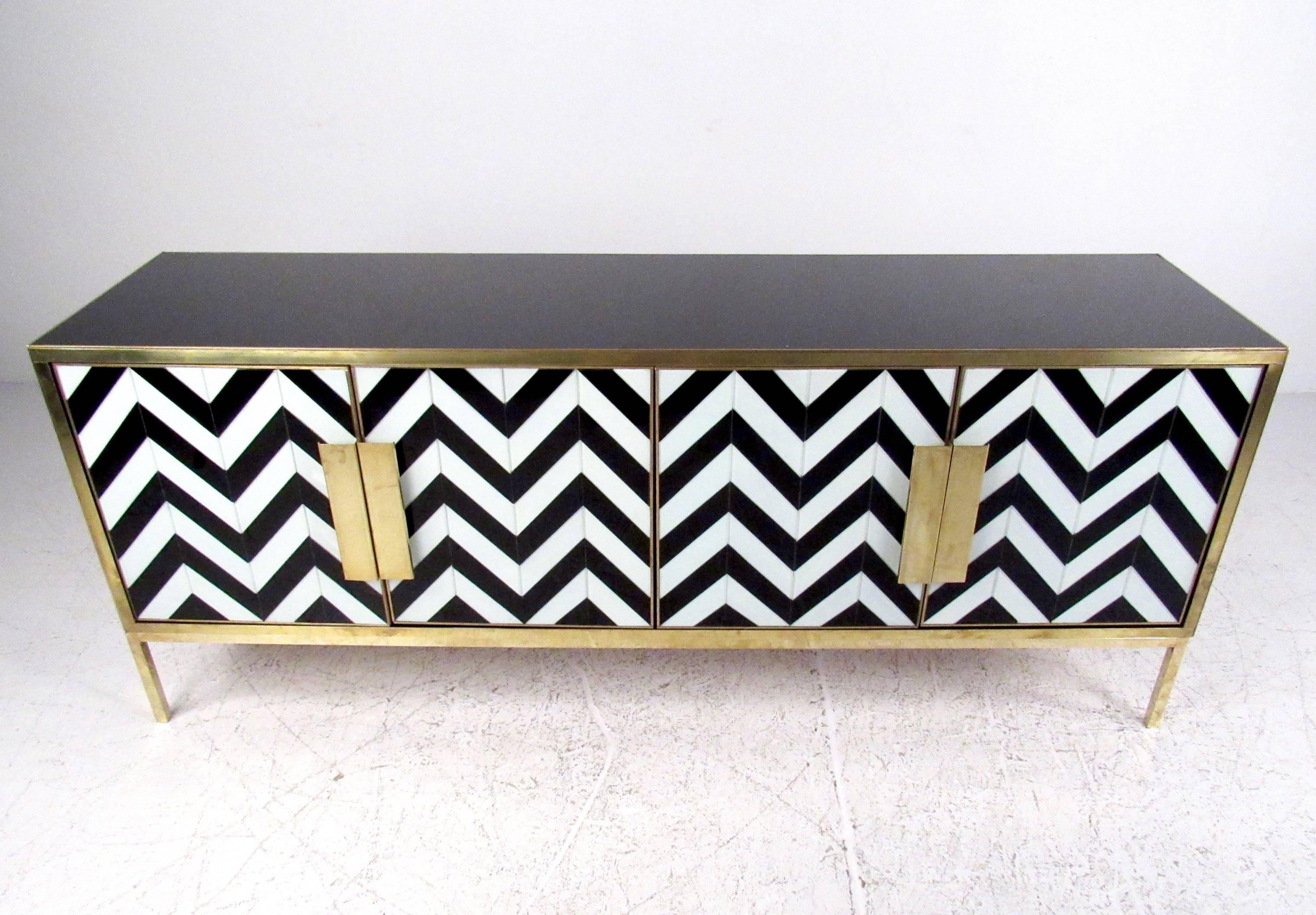 This Mid-Century Modern credenza features a unique Herringbone pattern underneath glass finish, with a painted black top/sides covered similarly in glass. The eye-catching black and white pattern is wonderfully accented by brass trim, legs, and