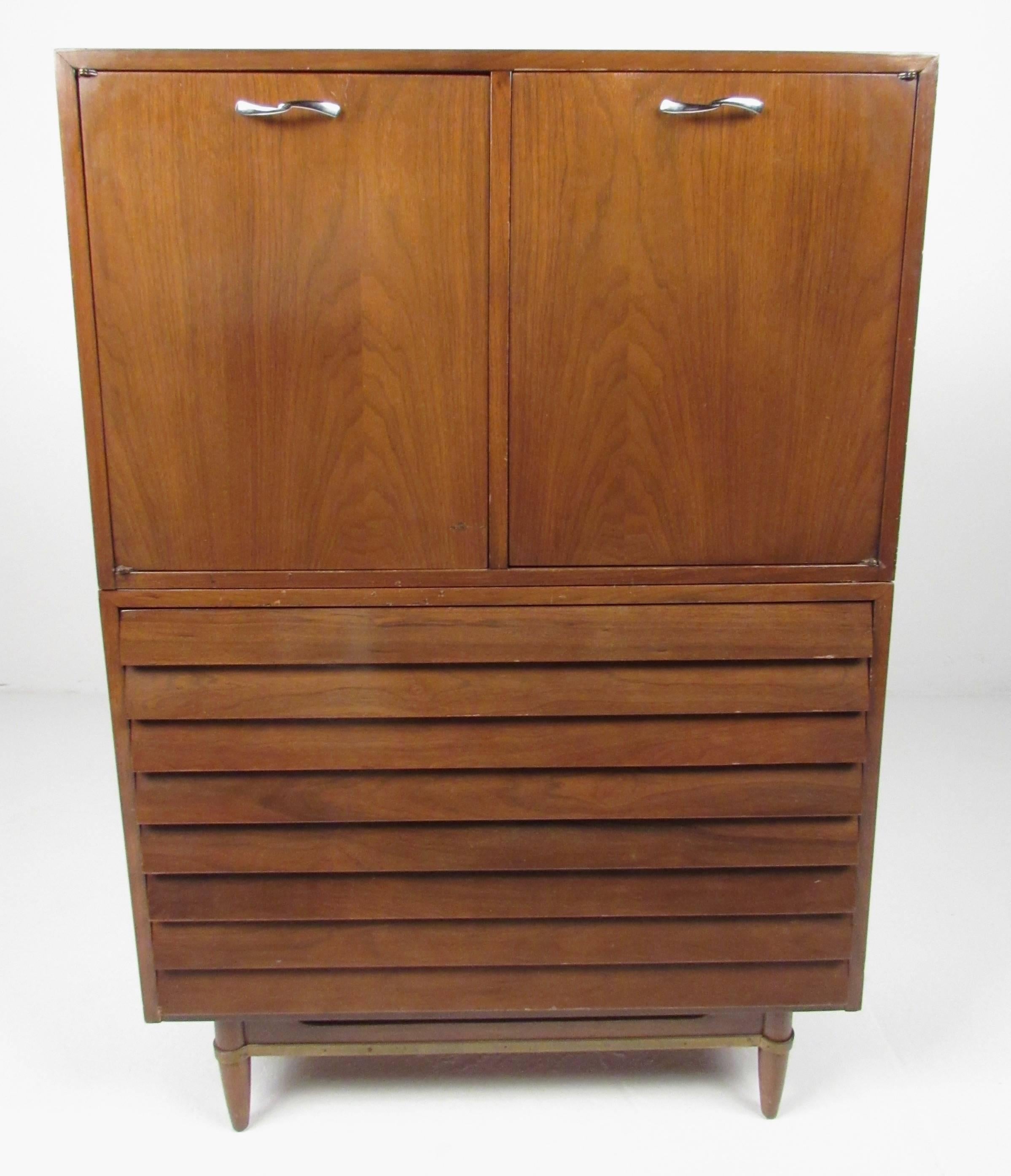 This vintage walnut dresser features two stacking cabinets with a mix of shelf and drawer storage. Mid-Century manufacturer American of Martinsville crafted this stylish highboy dresser with louvered front drawers, unique brass stretcher trim, and
